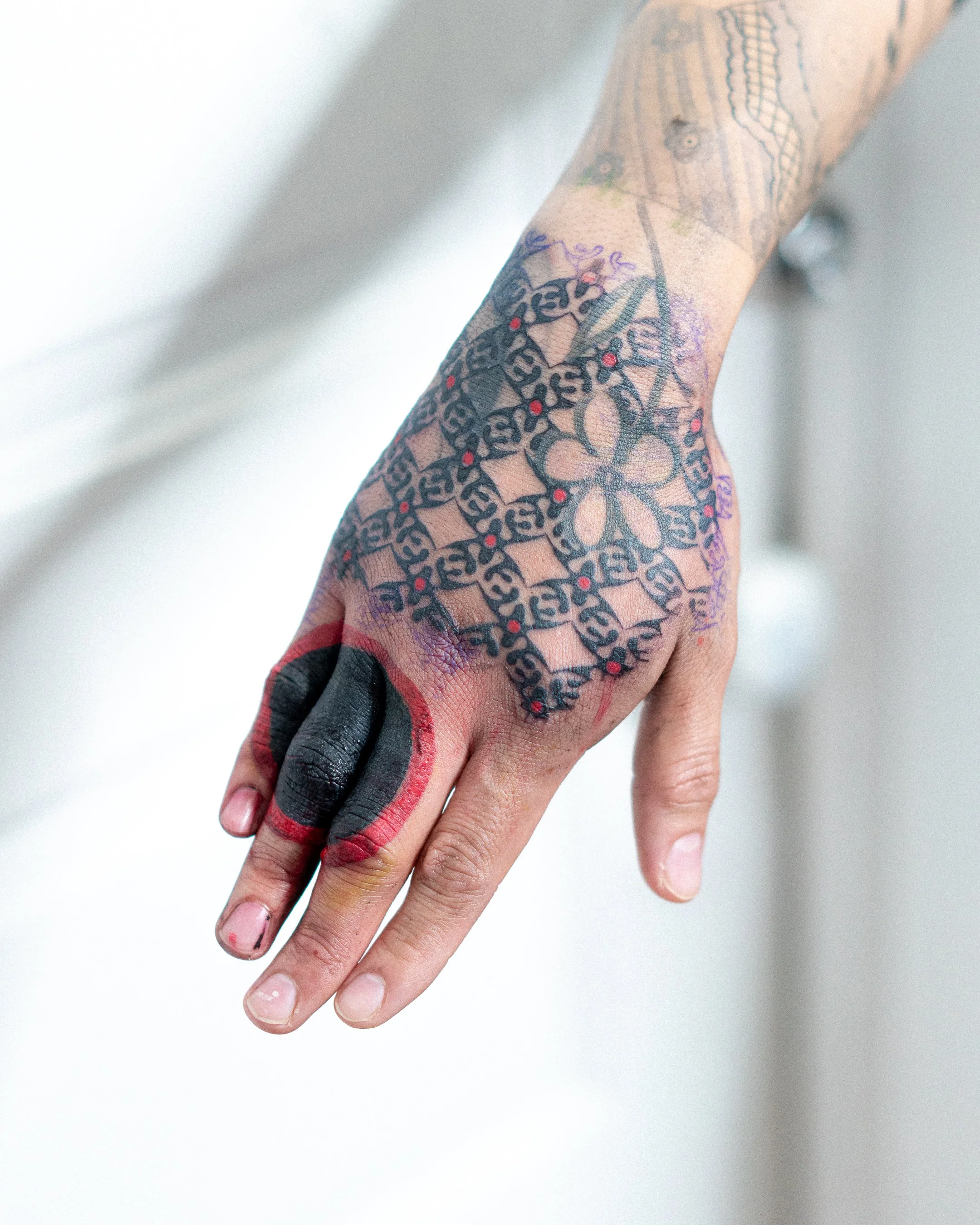 Poignet tatoué avec un tatouage complexe de style géométrique noir et rouge.