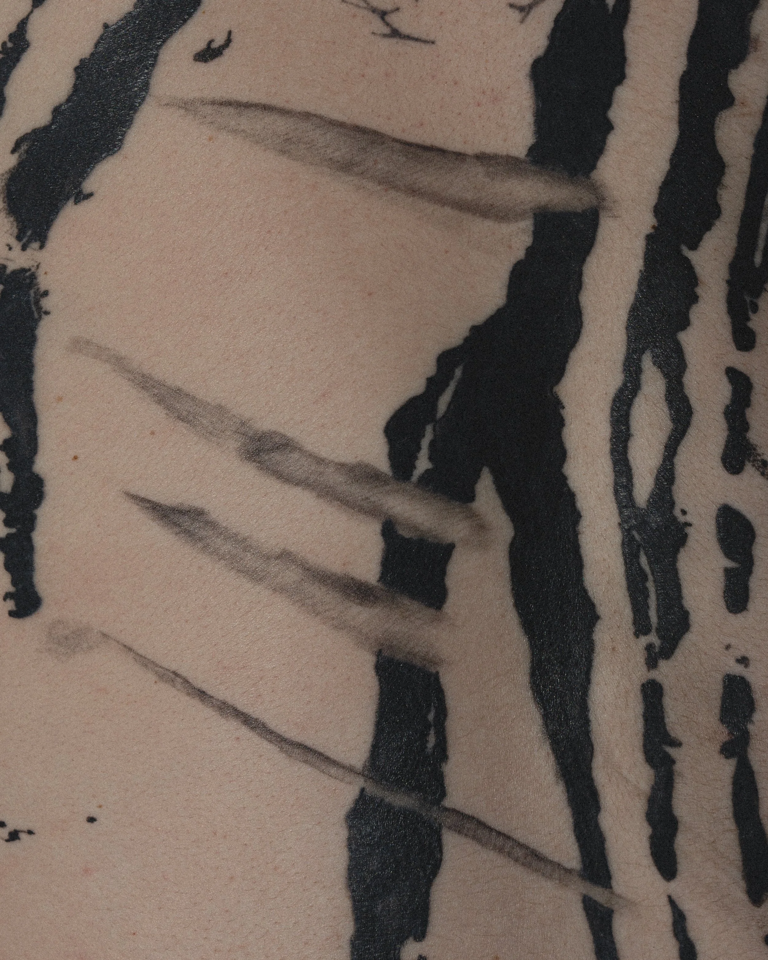 Tatouage d'une femme avec des motifs noirs et des lignes grises sur la peau.