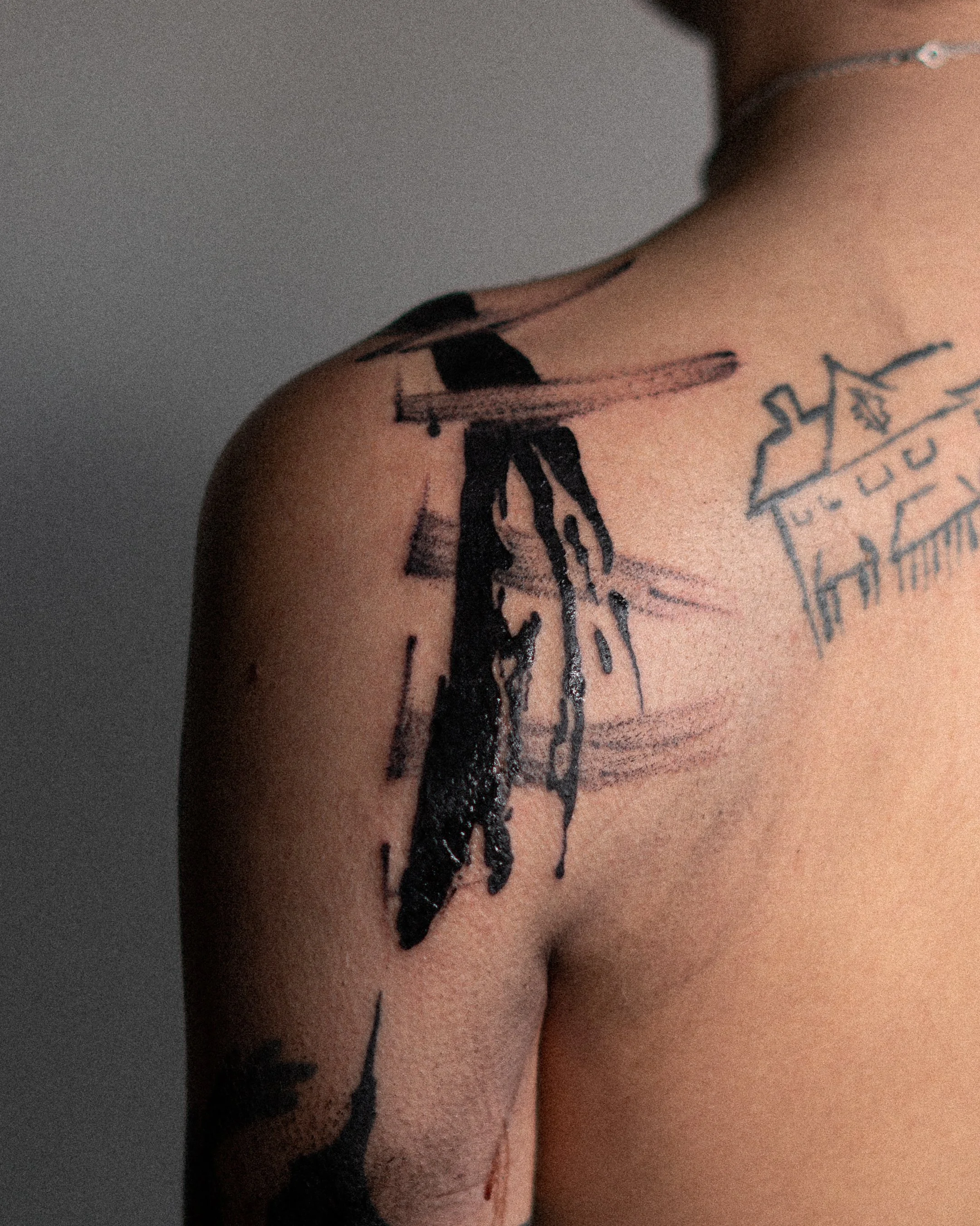 Tatouages noirs et dessins abstraits sur une épaule et une poitrine, y compris une étoile, une maison et des lignes scriptées.