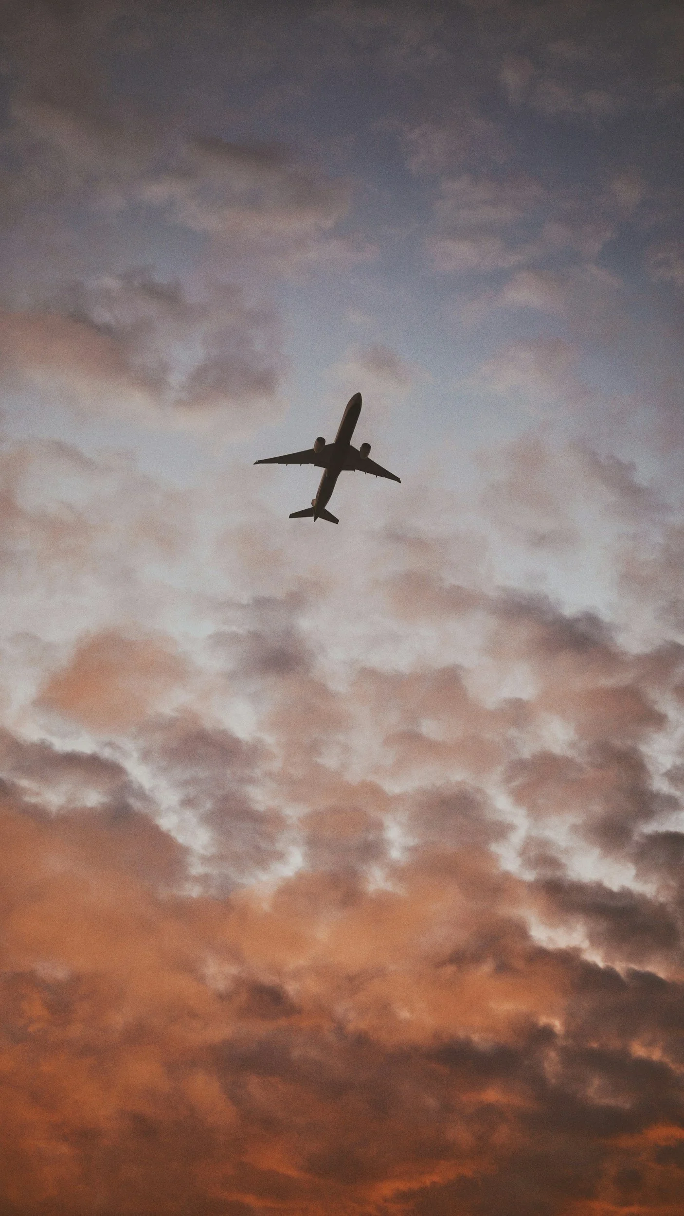 An airplane flying in the sky at sunset with pink and purple clouds.
