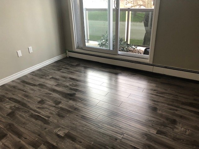 Empty room with dark wood laminate flooring, grey walls, and a large glass sliding door leading outside.