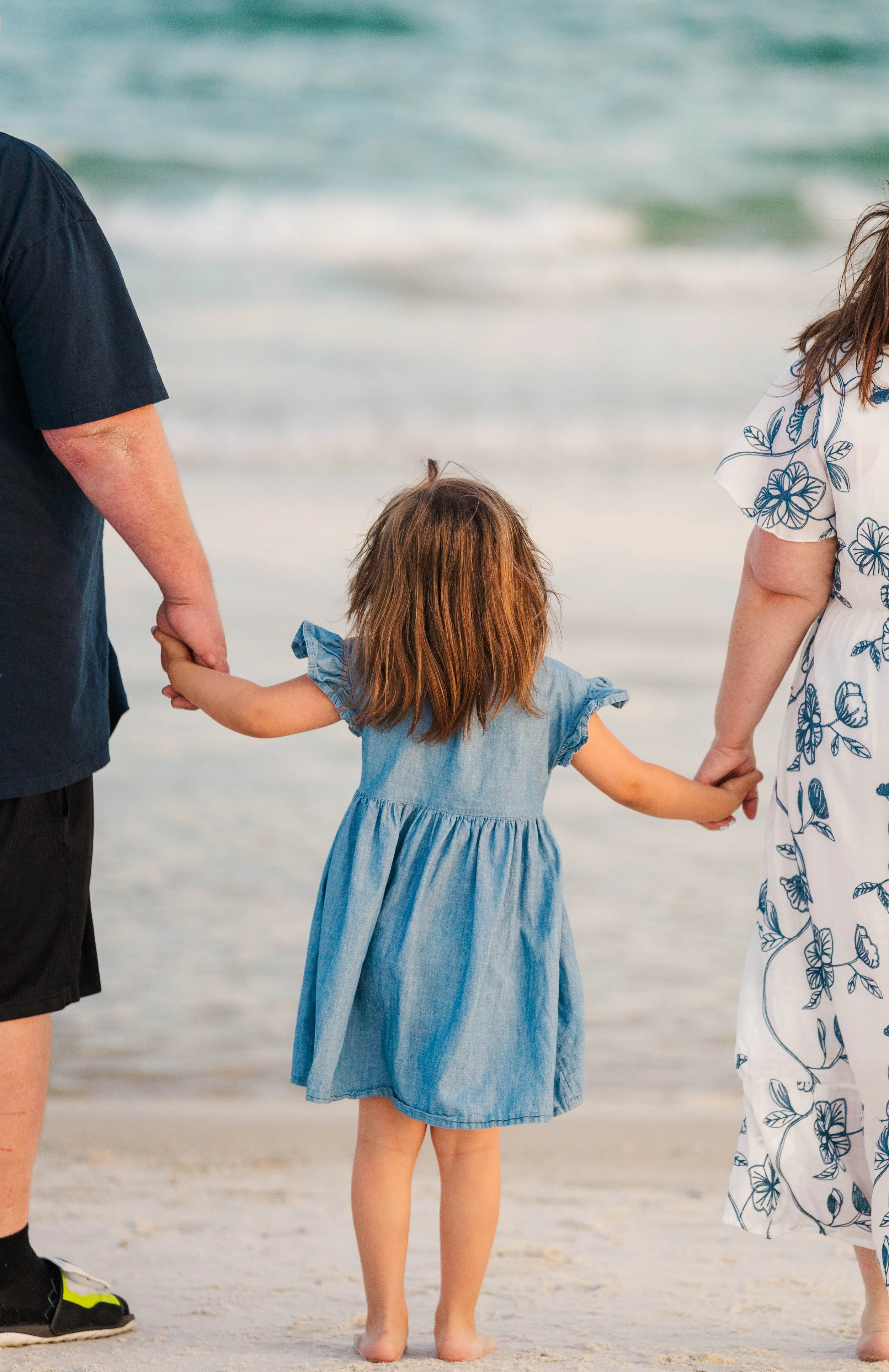 A mom, dad, and daughter sharing a sunset moment on the Gulf Shores beach during a family photography session by Mackenzie's Coastal Clicks in Orange Beach Alabama