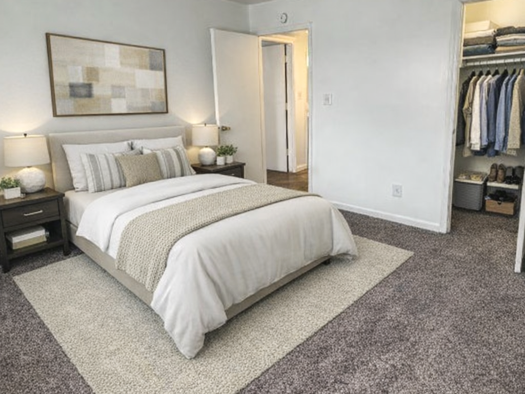 A bedroom with a bed, two nightstands with lamps, and an open closet with clothes.