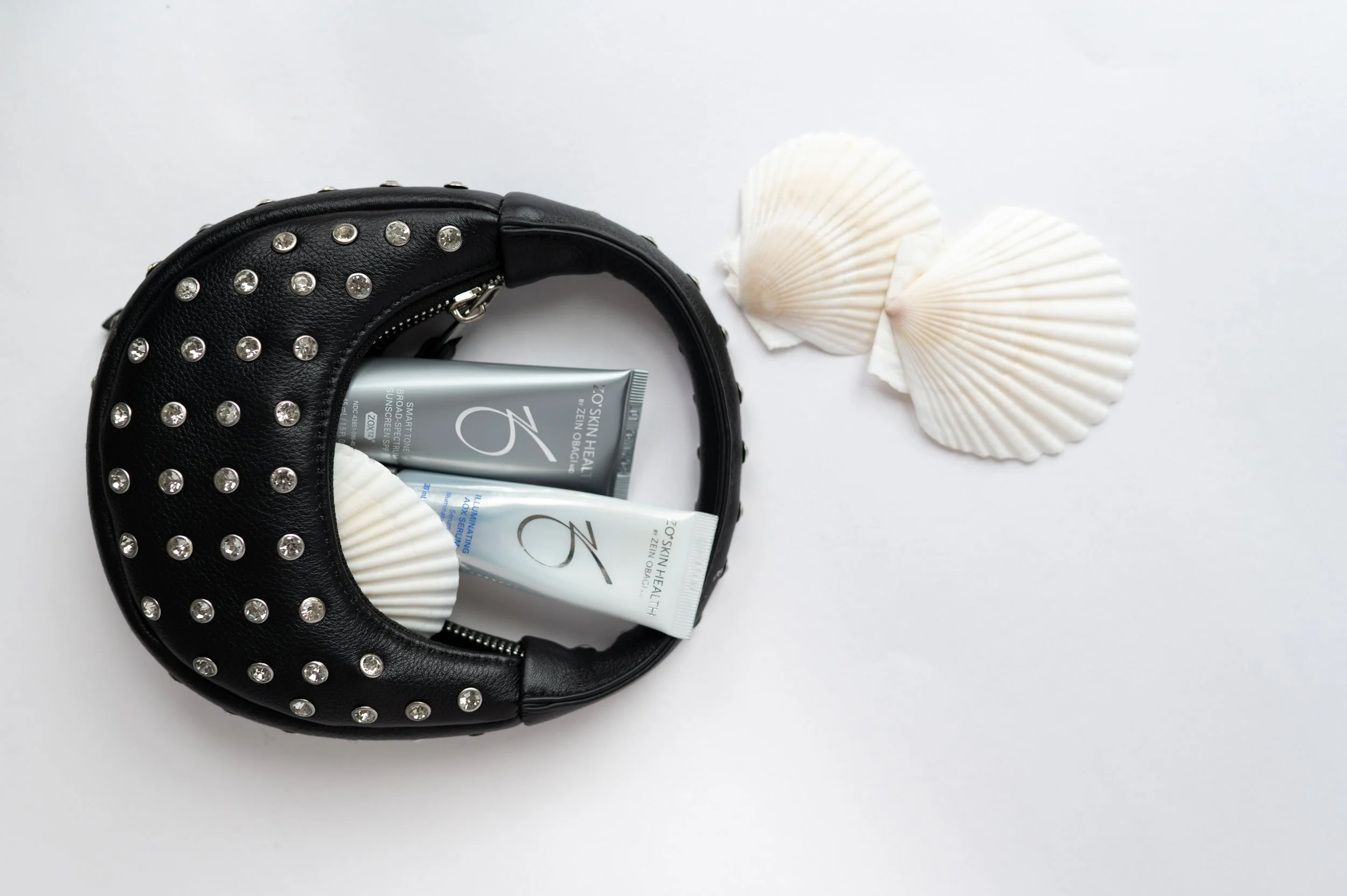 ZO Skin Health sunscreen products displayed in a black studded handbag with seashells for a summer skincare guide, highlighting daily SPF protection and medical-grade skincare.