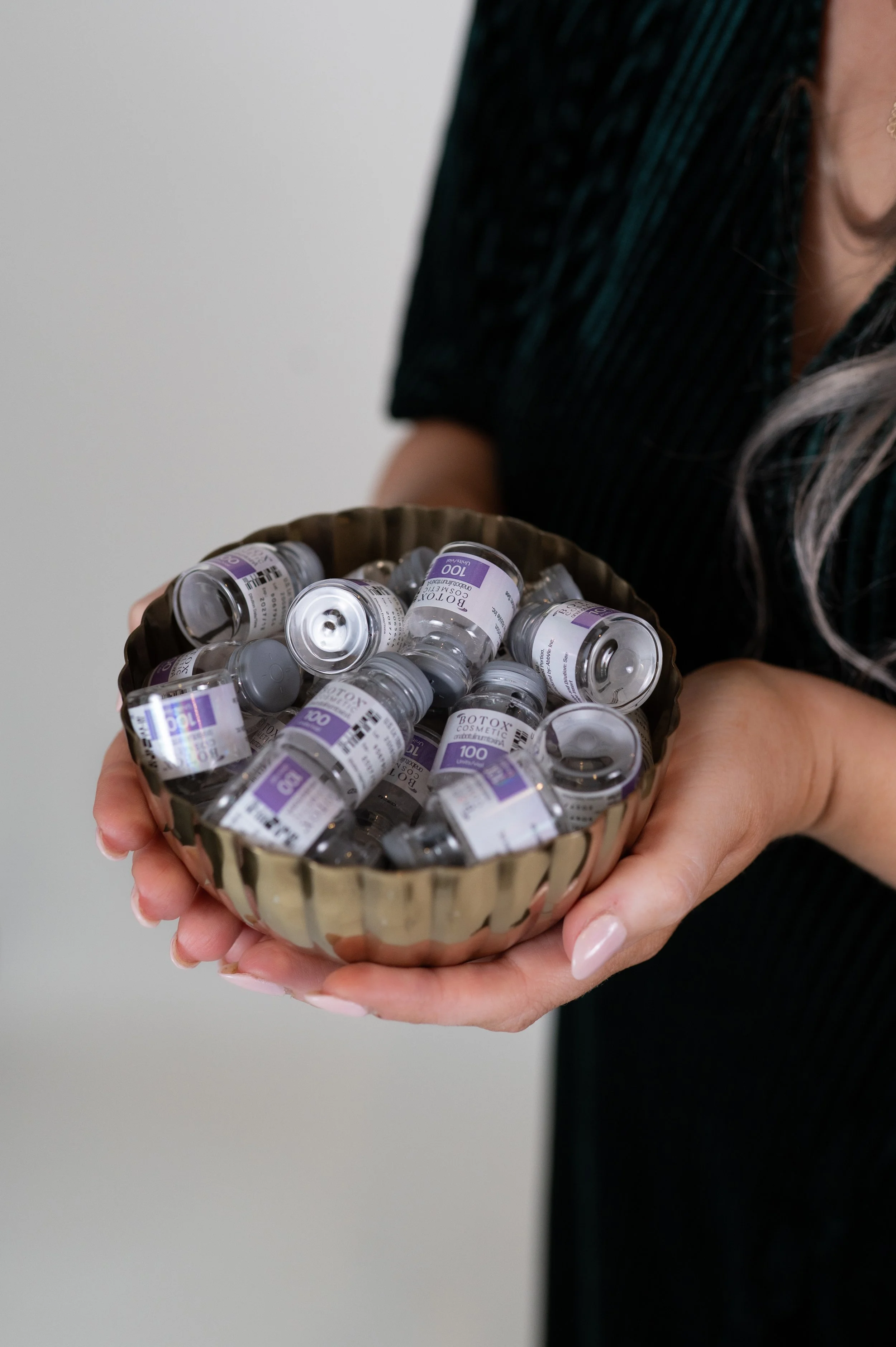 Hand holding a decorative bowl filled with small vials labeled 'Botox'