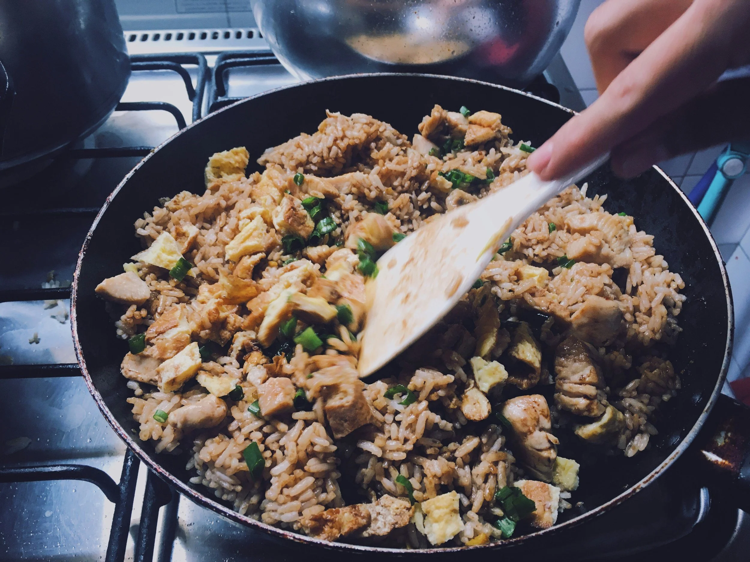 Stir-fried rice in a skillet with chopped green onions and pieces of chicken.