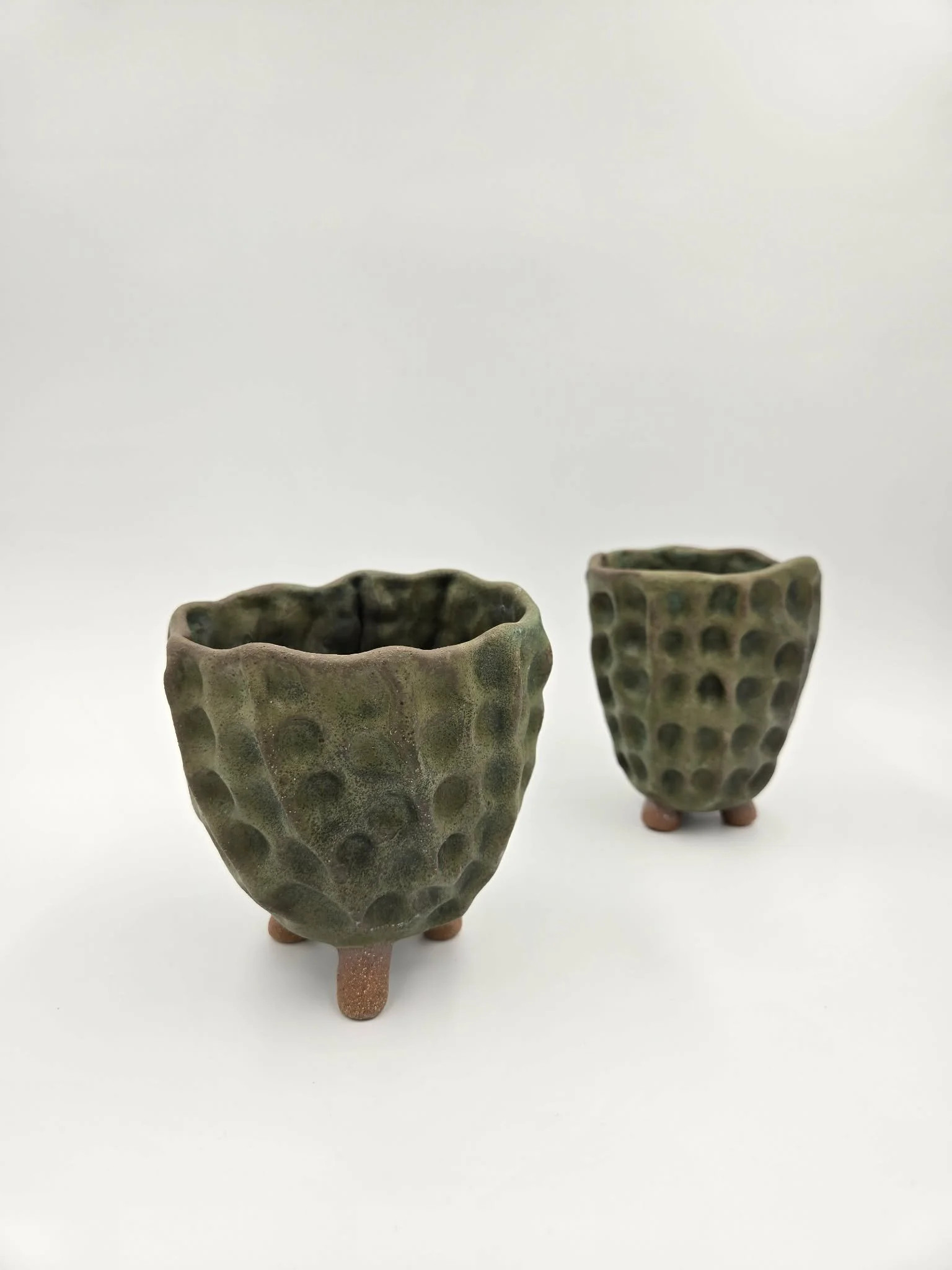 Deux poteries en céramique avec une surface texturée en forme de nid d'abeilles, chacune sur trois petits pieds en terre cuite, placées sur un fond blanc.