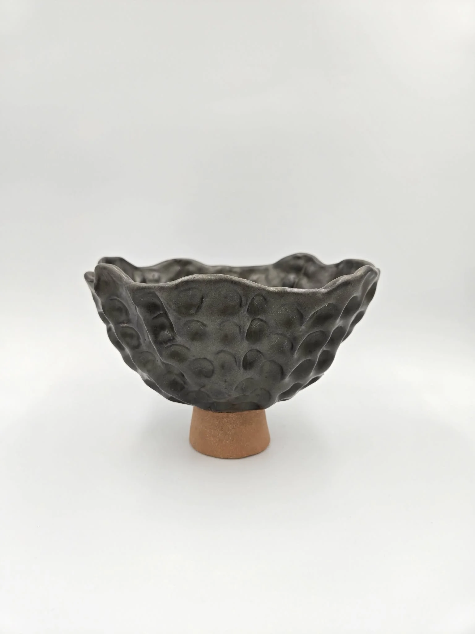 Bol en céramique gris avec un motif ondulé, posé sur un support en terre cuite, sur fond blanc.