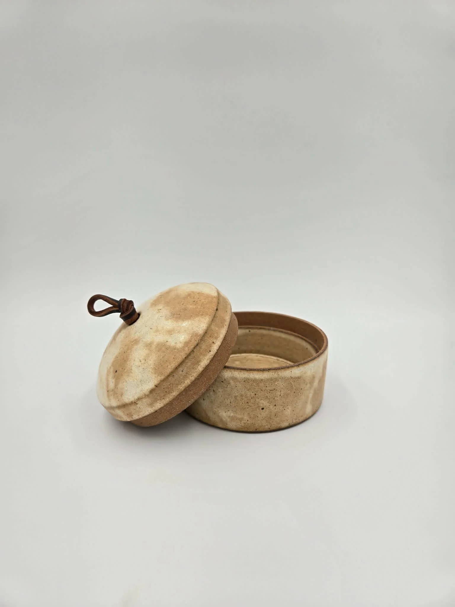 Boîte en céramique beige avec couvercle et un nœud en cuir sur le couvercle.