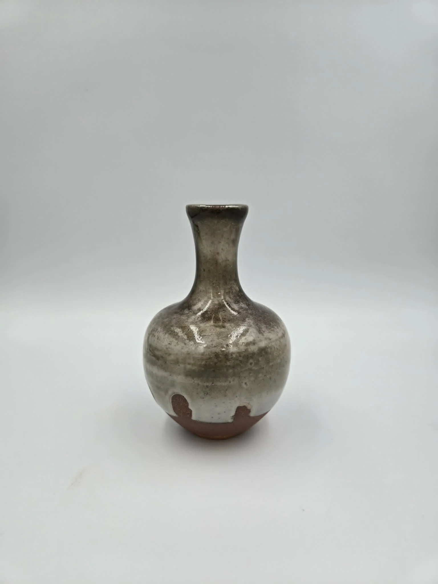 Petit vase en céramique avec un cou étroit, en relief et avec un motif rouge en bas, posé sur un fond blanc.