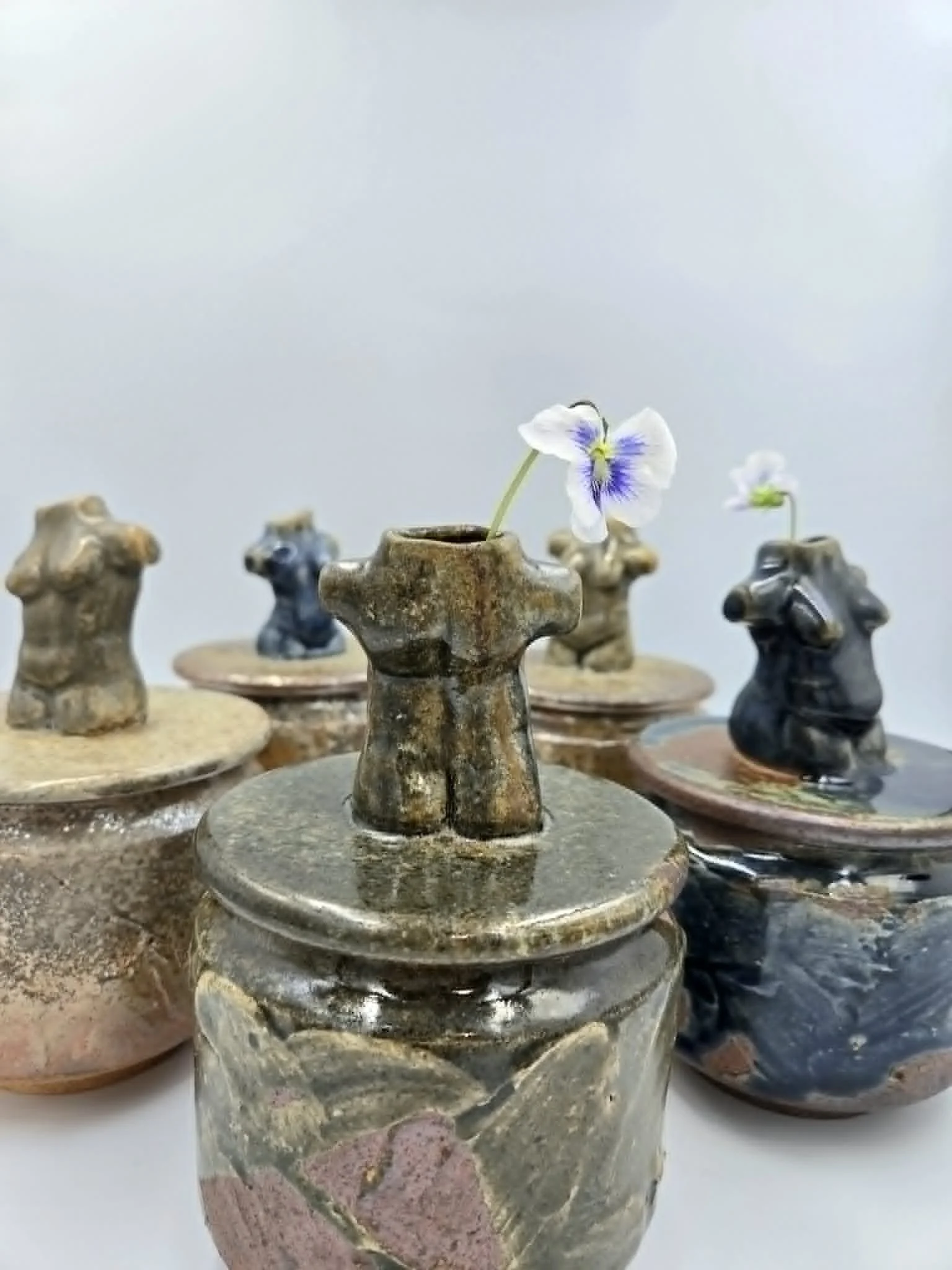 Petites vases en céramique avec des fleurs violettes et blanches, placées sur une surface en pierre.