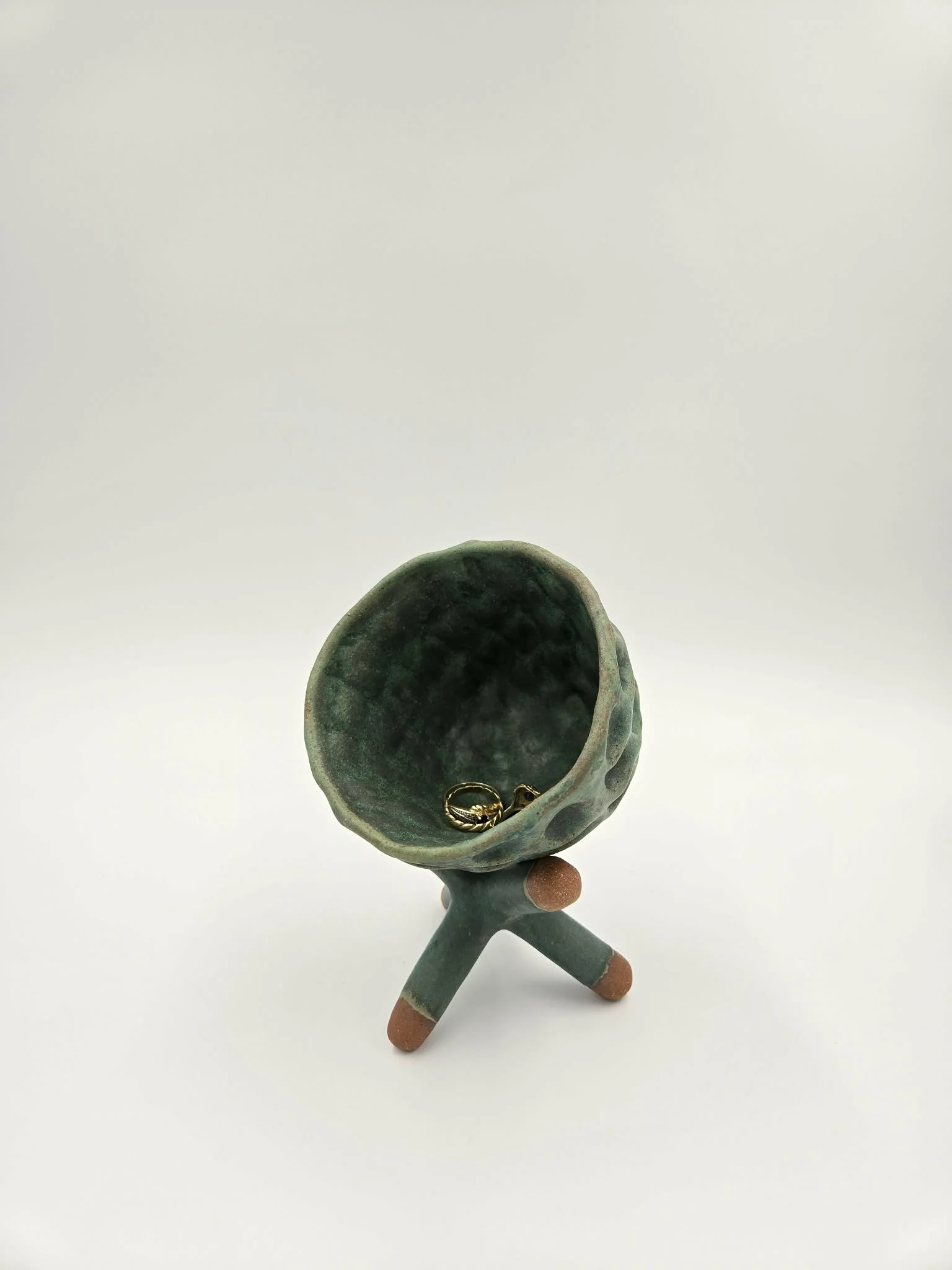 Une boîte en céramique en forme de tête ouverte contenant une bague en or. La boîte repose sur une petite sculpture en forme de bras avec des pieds