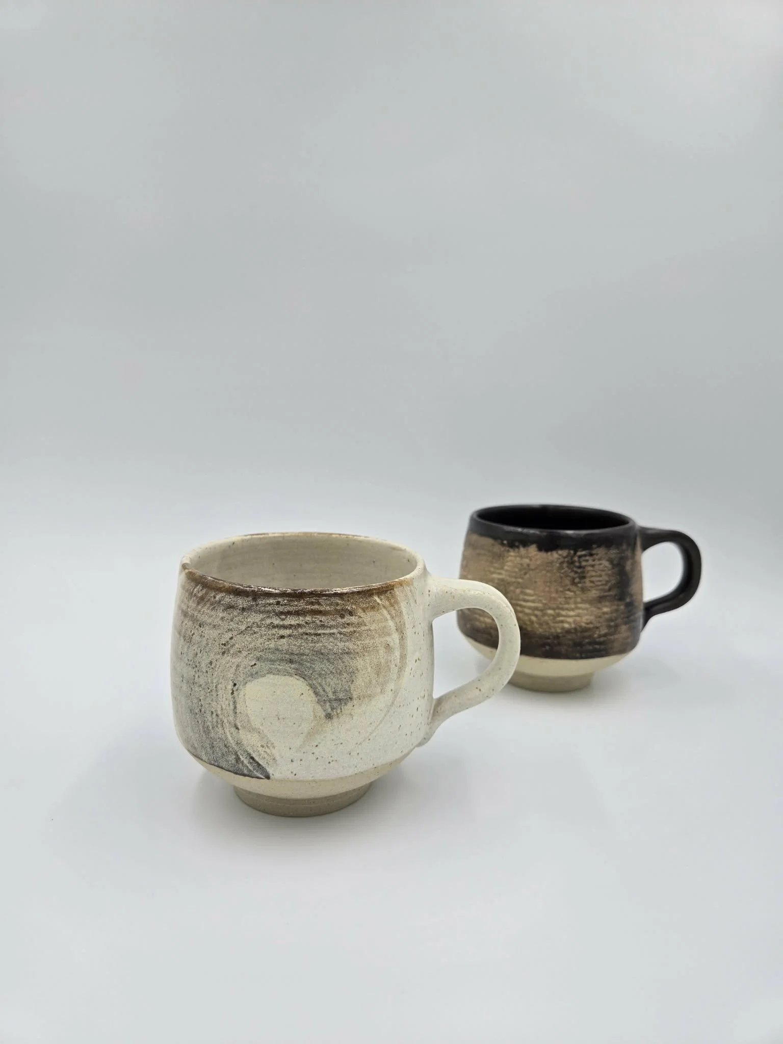 Deux tasses en céramique artisanale avec un design écologique sur fond blanc.