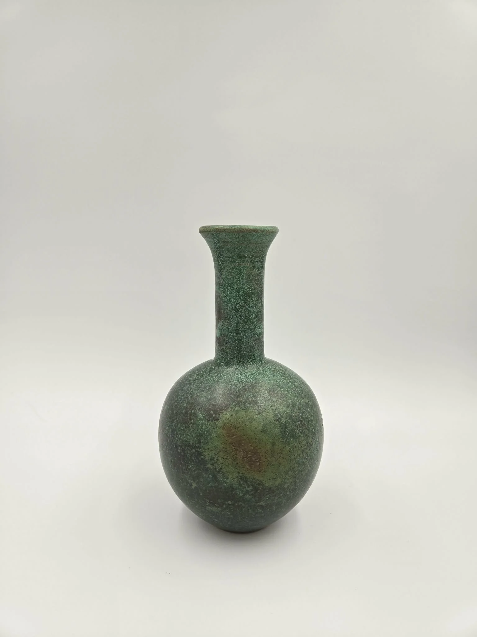 Une petite vase en céramique verte avec une texture rugueuse, posée sur un fond blanc