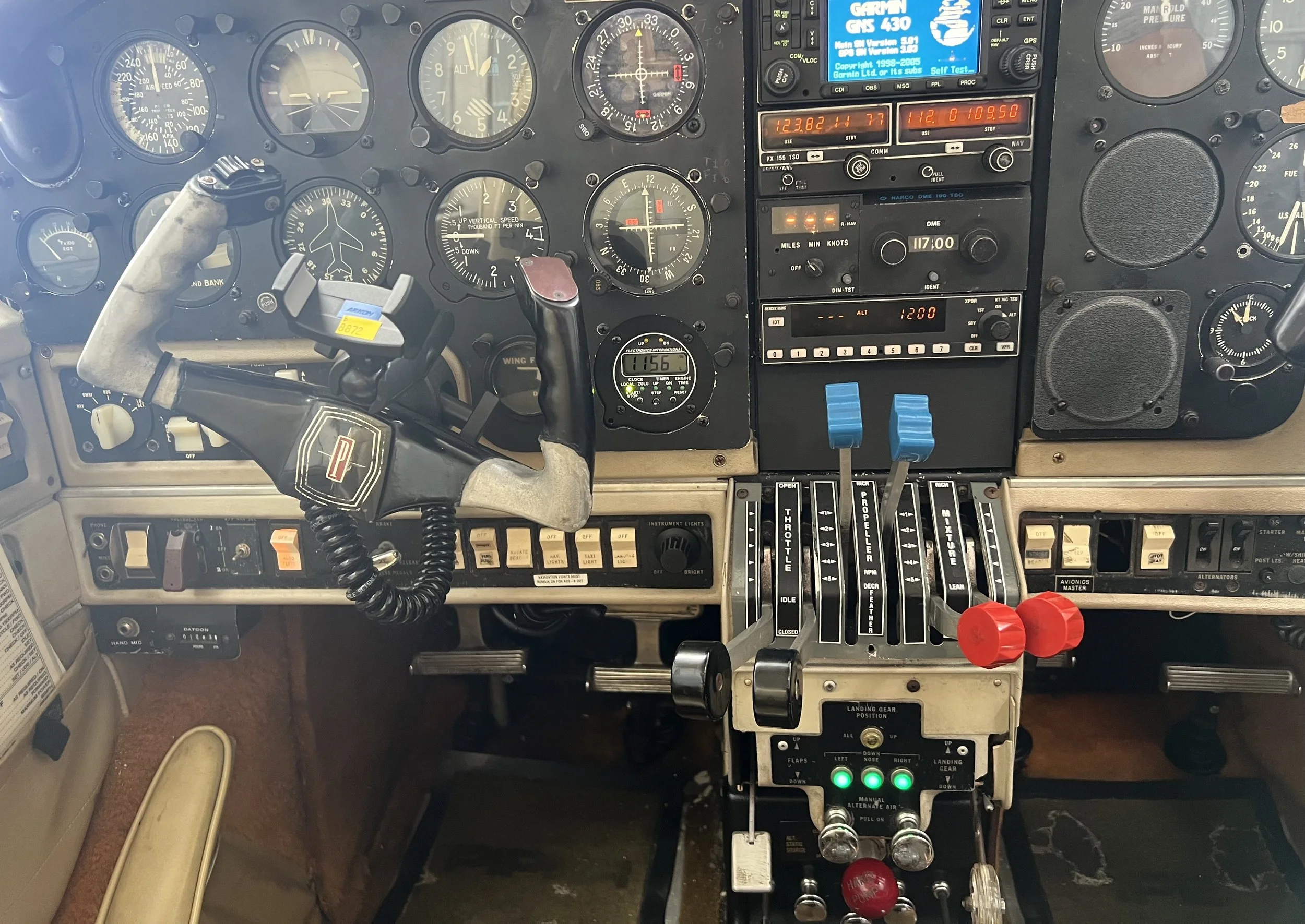 The cockpit of an aircraft with various instruments, gauges, switches, and controls including throttle levers, radios, and autopilot indicators.