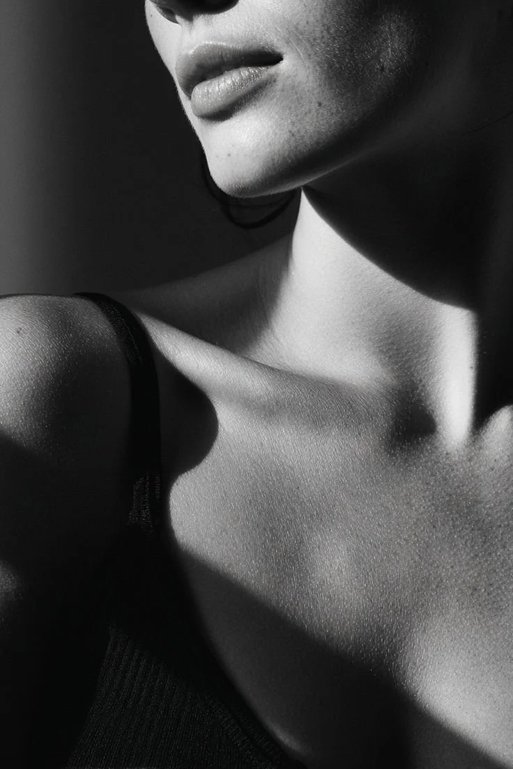 Close-up of a woman's face, shoulder, and collarbone in black and white, with dramatic shadowing.