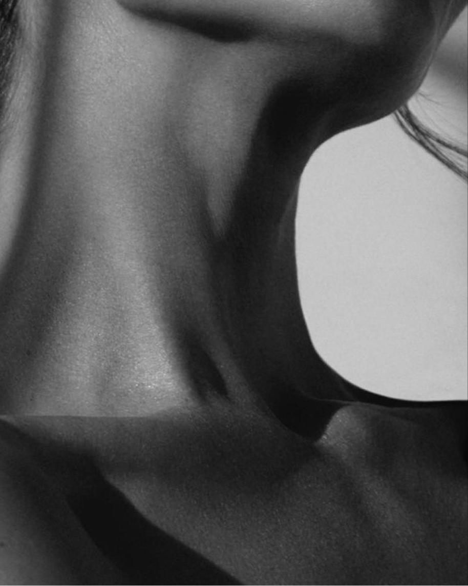 Close-up black and white photograph of a person's neck and shoulder, with a focus on the skin's texture and contours.