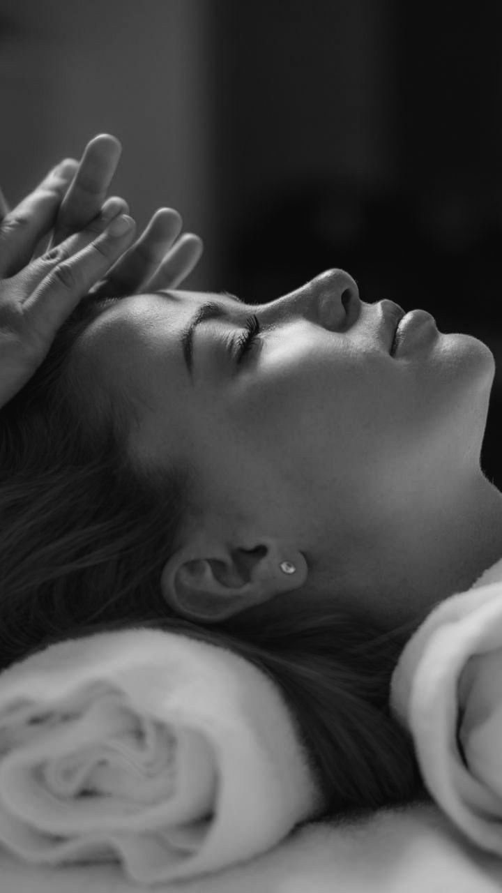 A woman lying down with eyes closed, gently touching her forehead with her hand, in a peaceful pose.