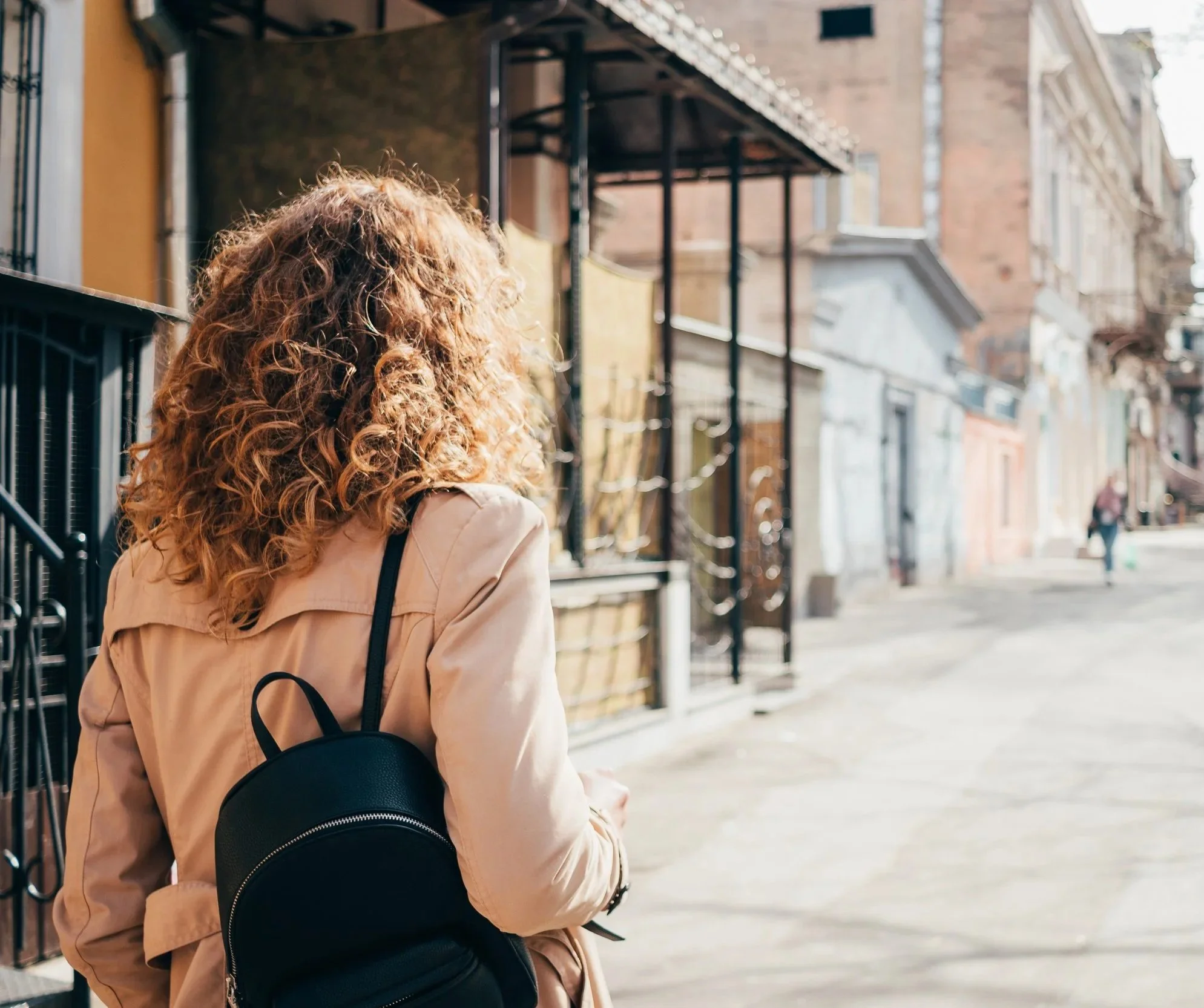 Rear view of curly hair woman in a trech coat walking down the street
