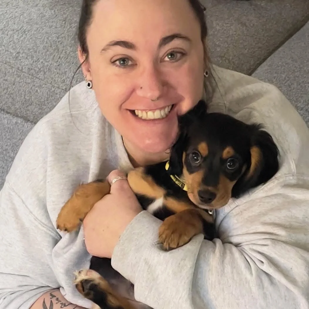 A woman smiling and holding a small black and tan dachshund puppy.