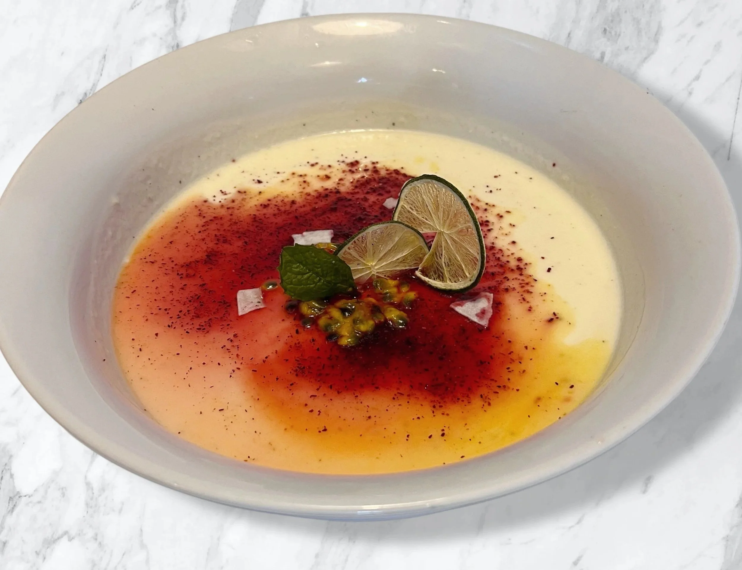 cardamom yogurt cream dessert garnished with hibiscus dust passionfruit juice coconut flakes and lime wheel
