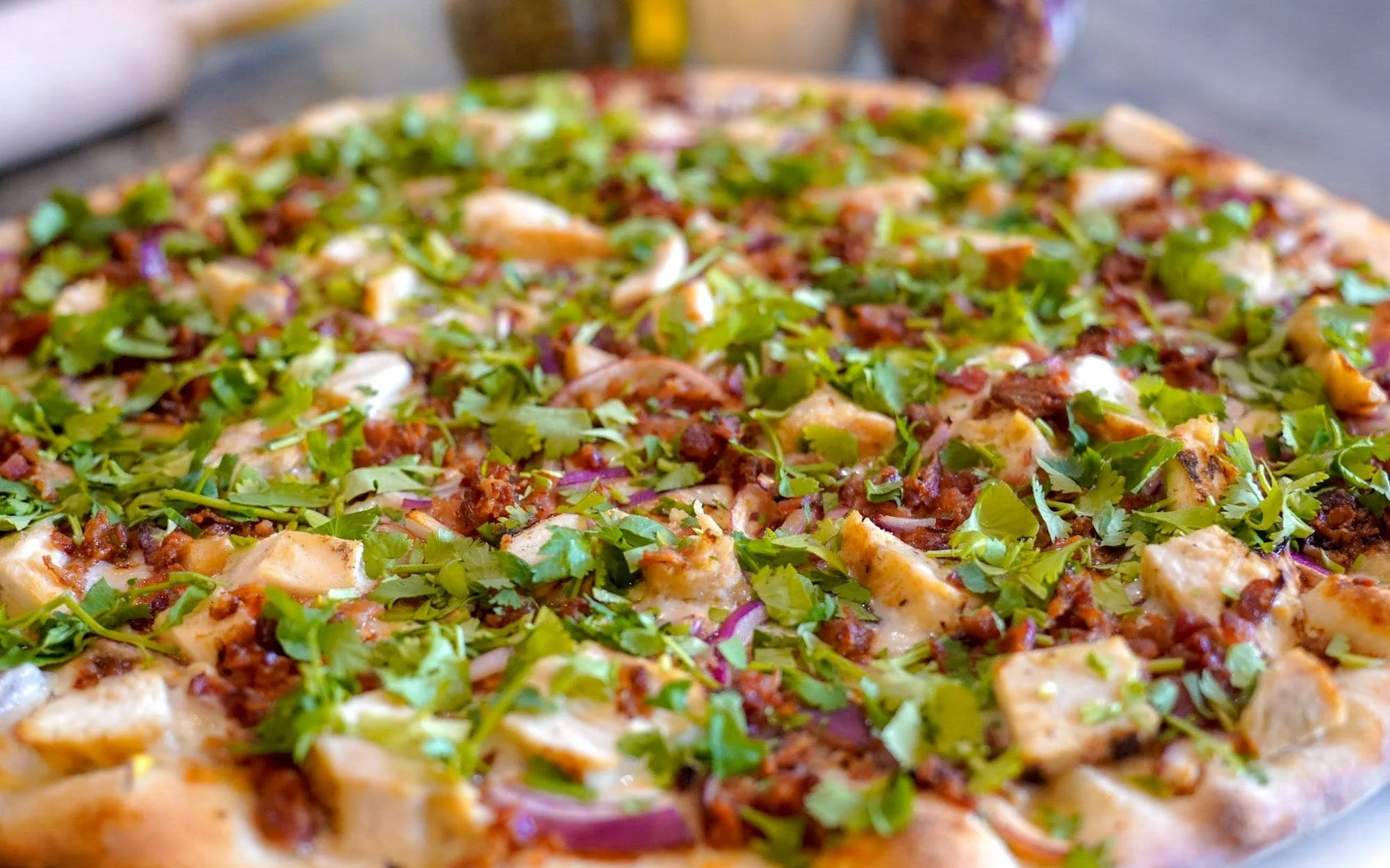 Close-up of a freshly baked pizza topped with leafy greens, cooked meats, and cheese.