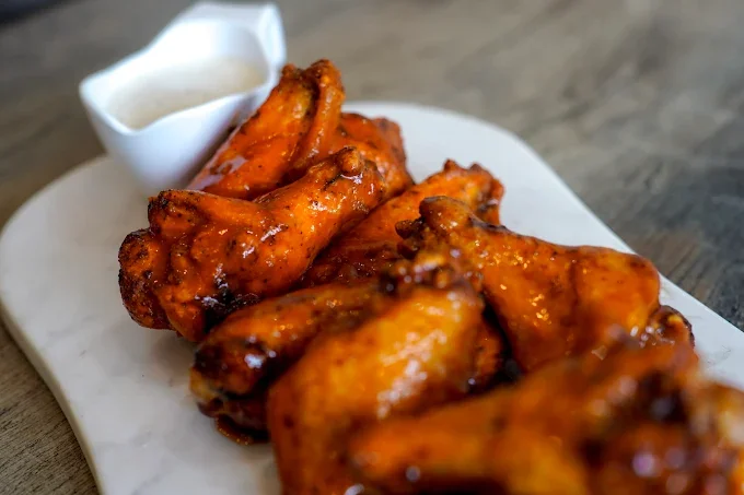 Close-up of glazed chicken wings with a side of ranch dipping sauce.