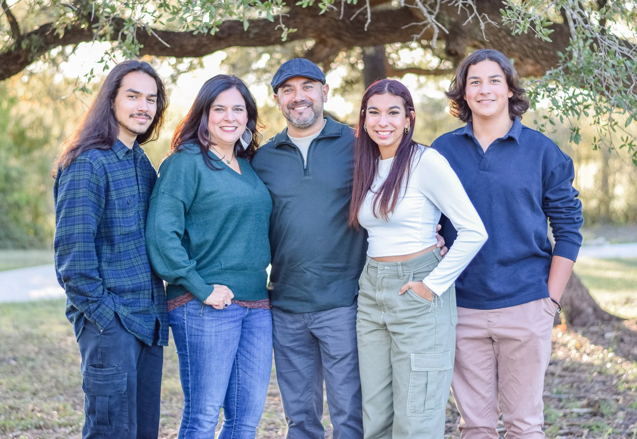 Group of five diverse people smiling and standing together outdoors under a large tree in a park.