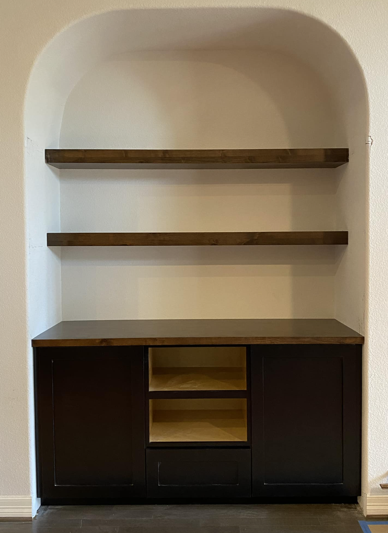 Empty built-in wall cabinet with two wooden shelves and black lower cabinet with open and closed storage.