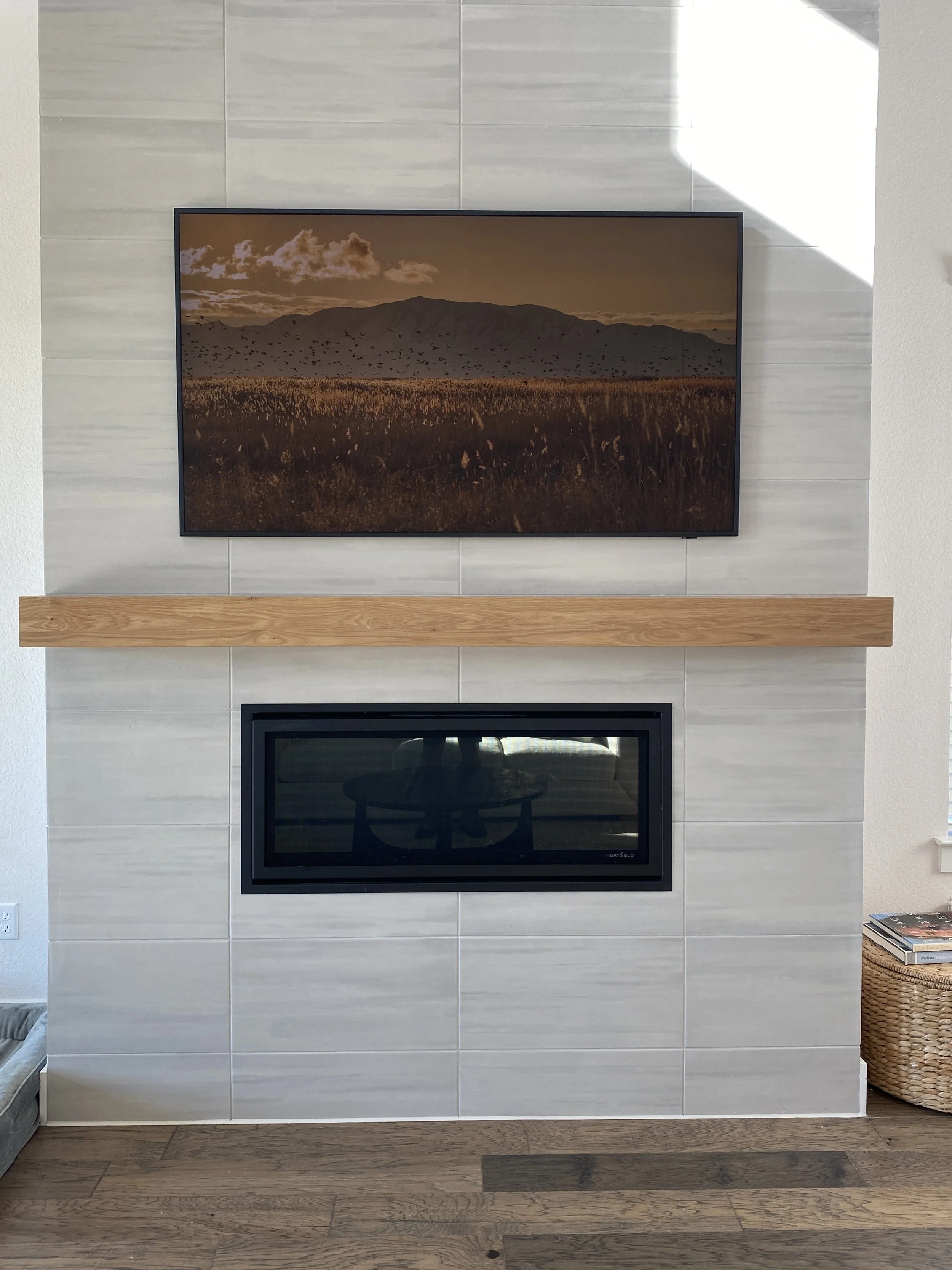 Living room fireplace with a mounted flat-screen TV displaying a landscape scene of a mountain, a cloudy sky, and a field with birds flying.