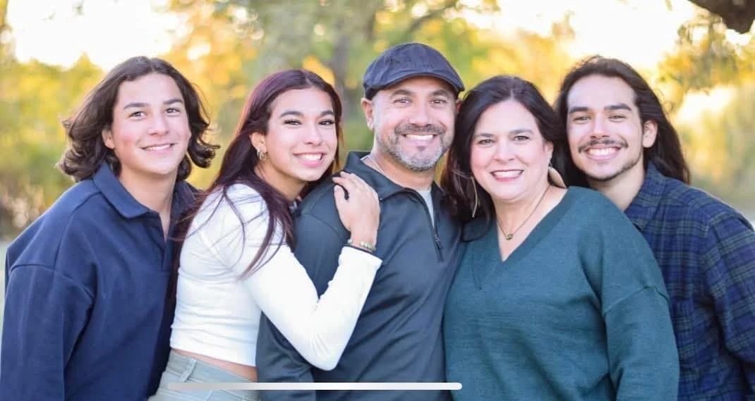A family of six smiling outdoors in a park during autumn.