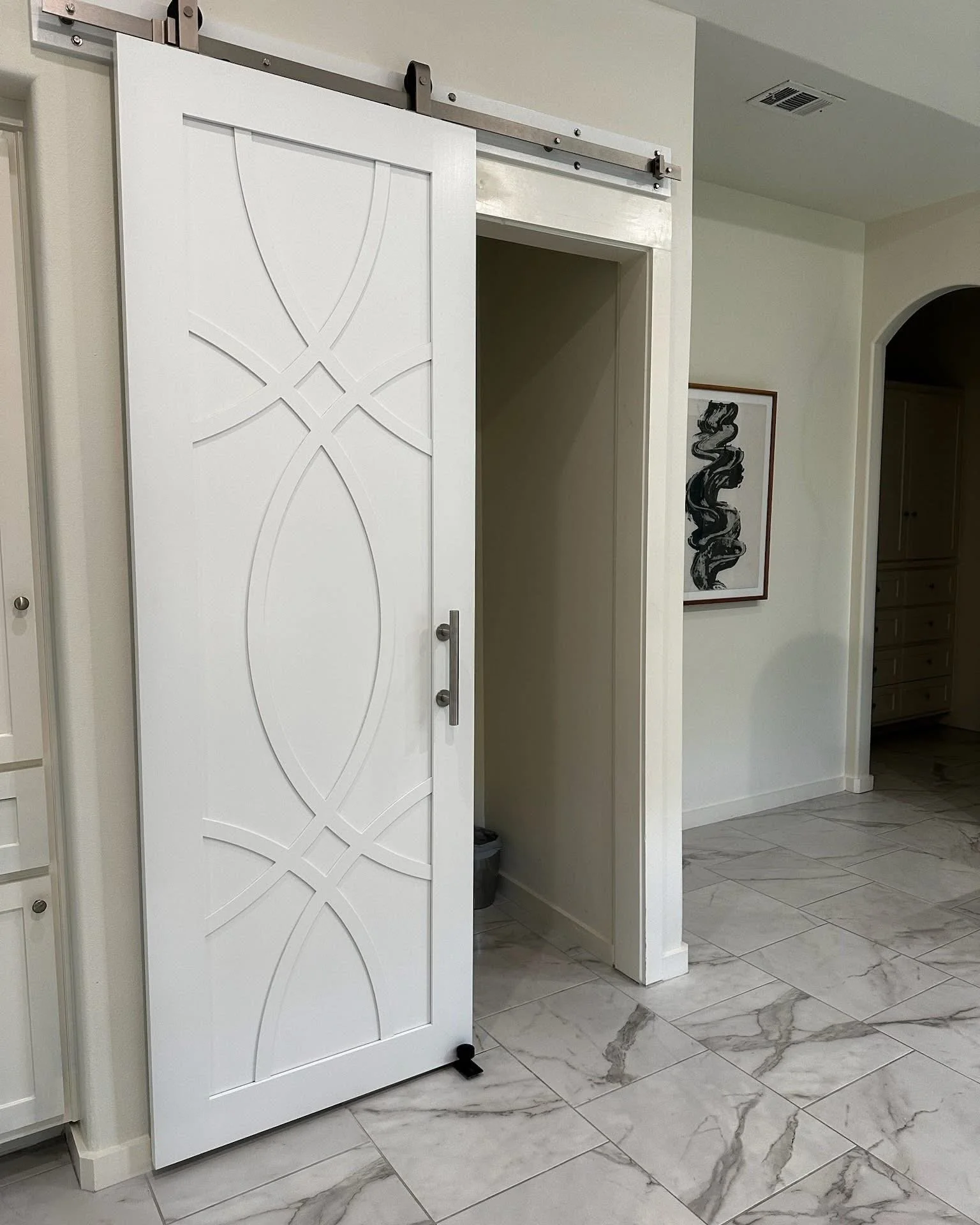 A sliding barn door on a metal track in a modern interior with white walls and marble flooring.
