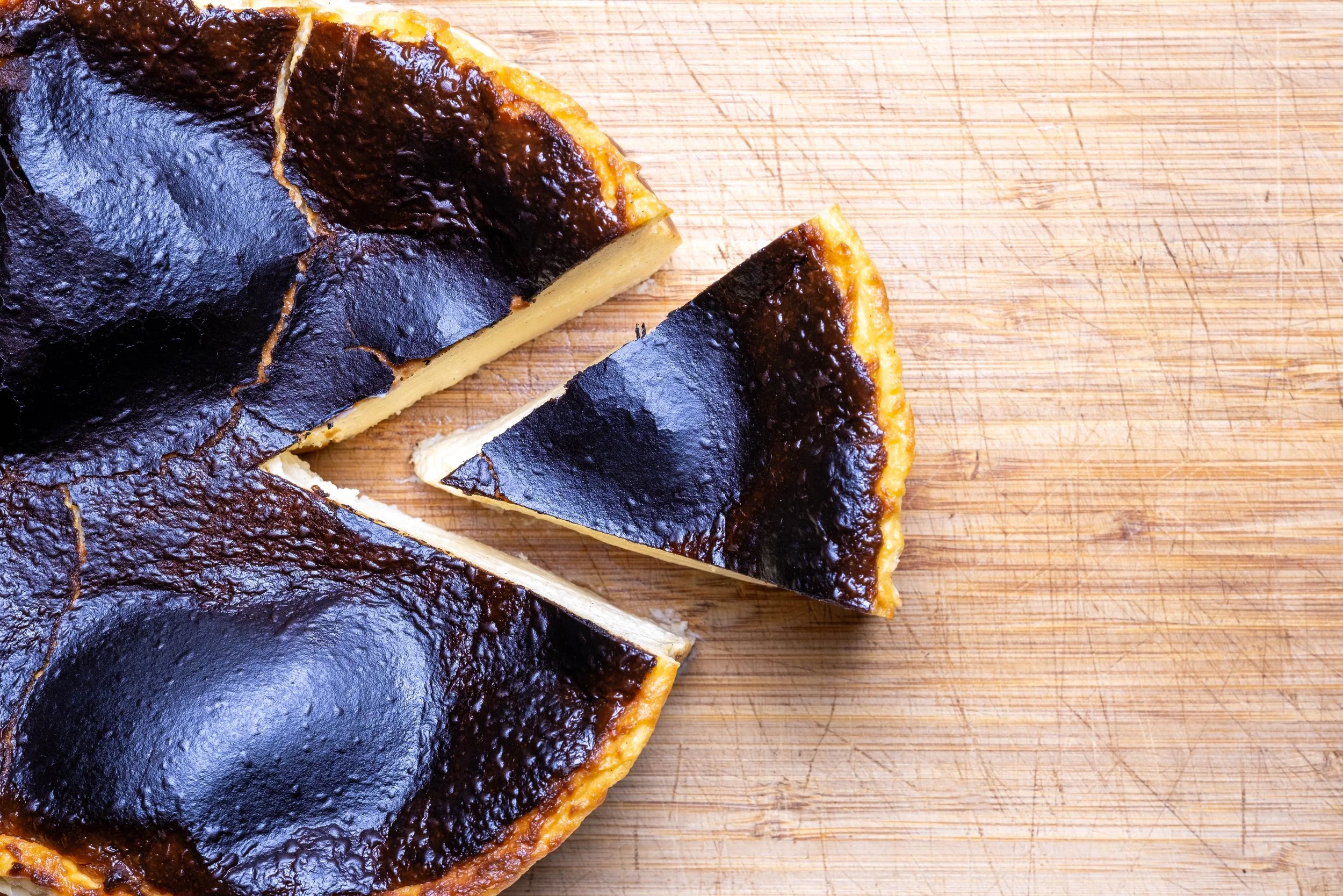 A sliced cheesecake with a dark, glossy topping on a wooden cutting board.