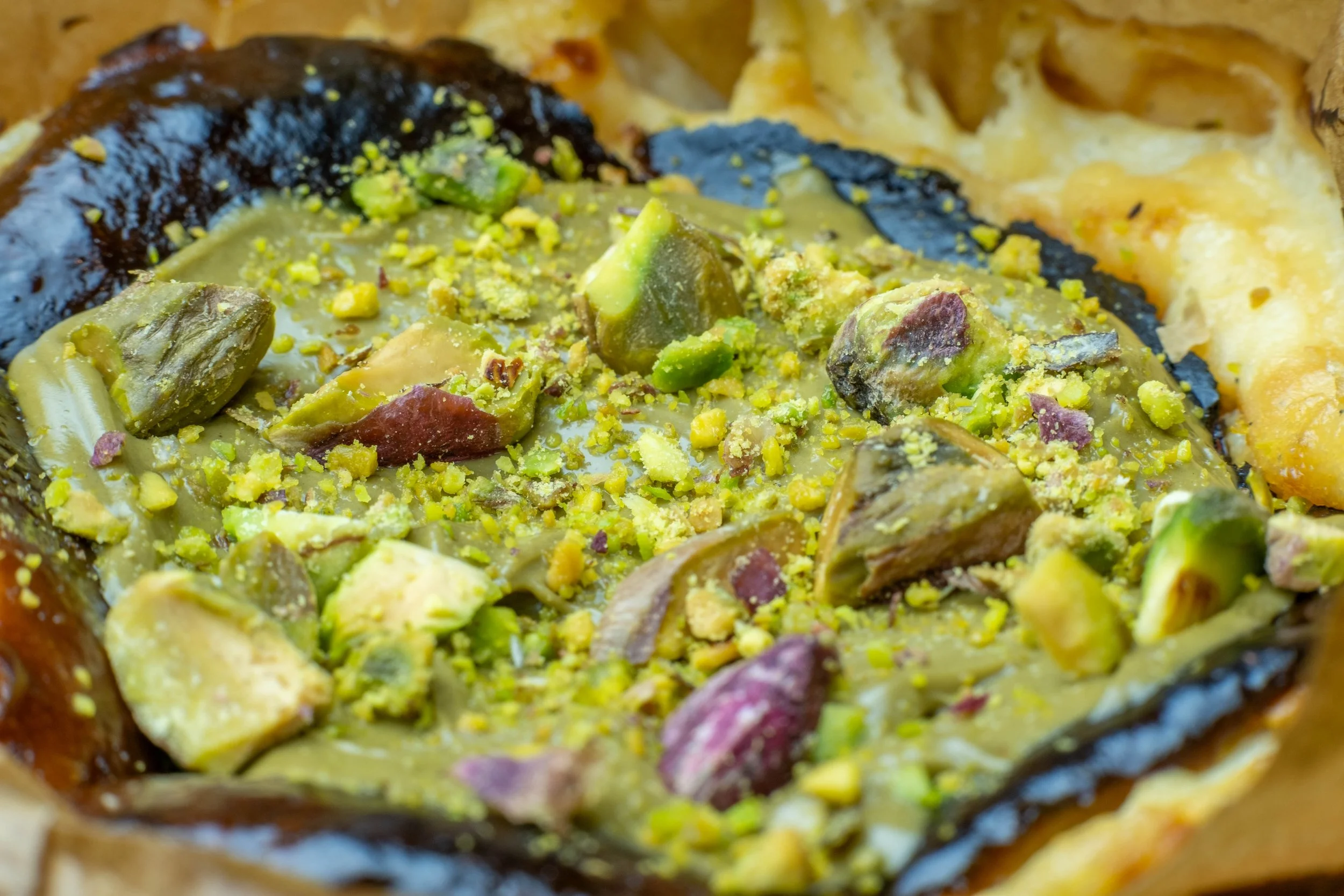Close-up of assorted pistachio nuts, some coated with chocolate, on a baked dessert or pastry.