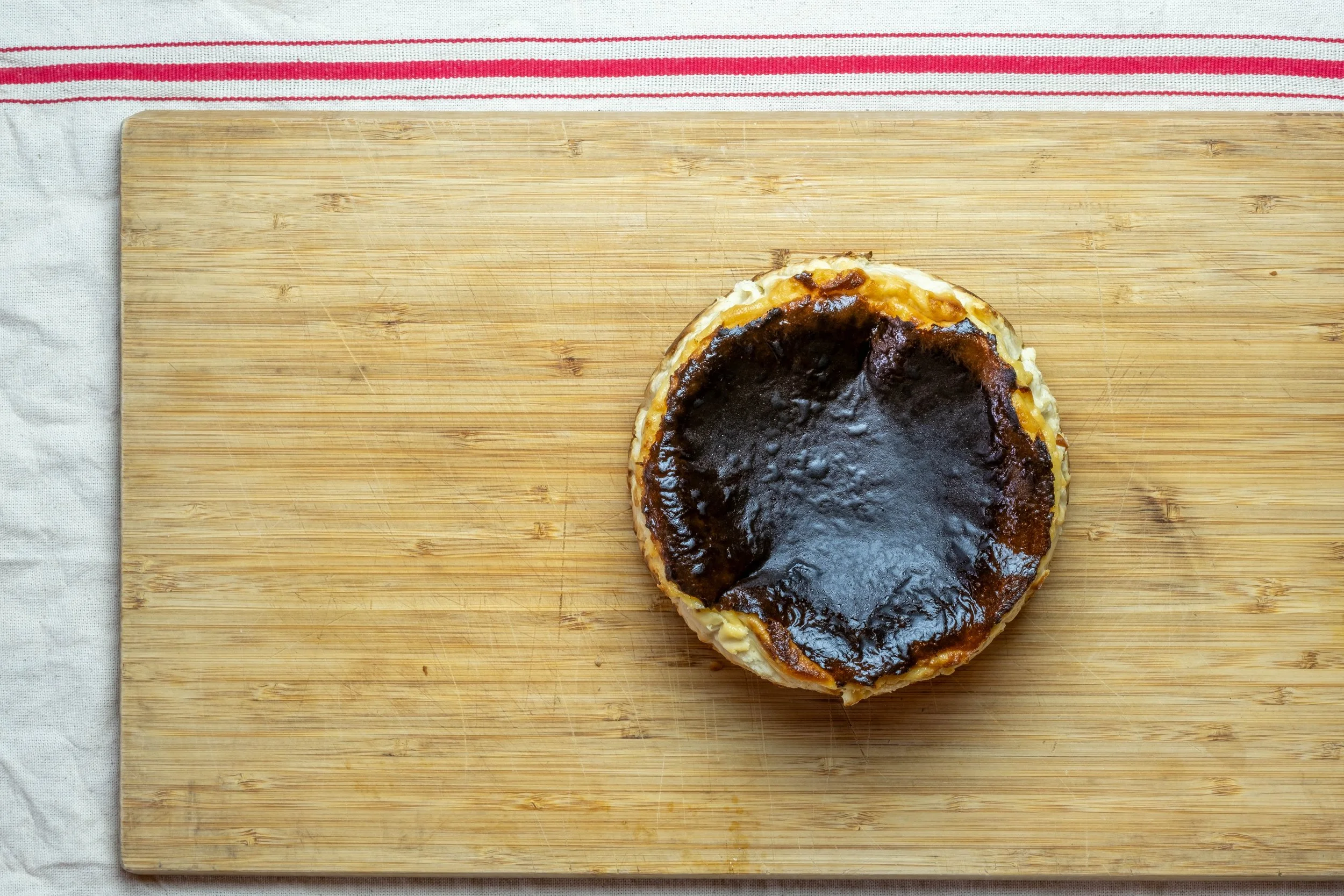 A partially eaten chocolate tart on a wooden cutting board with a striped cloth underneath.