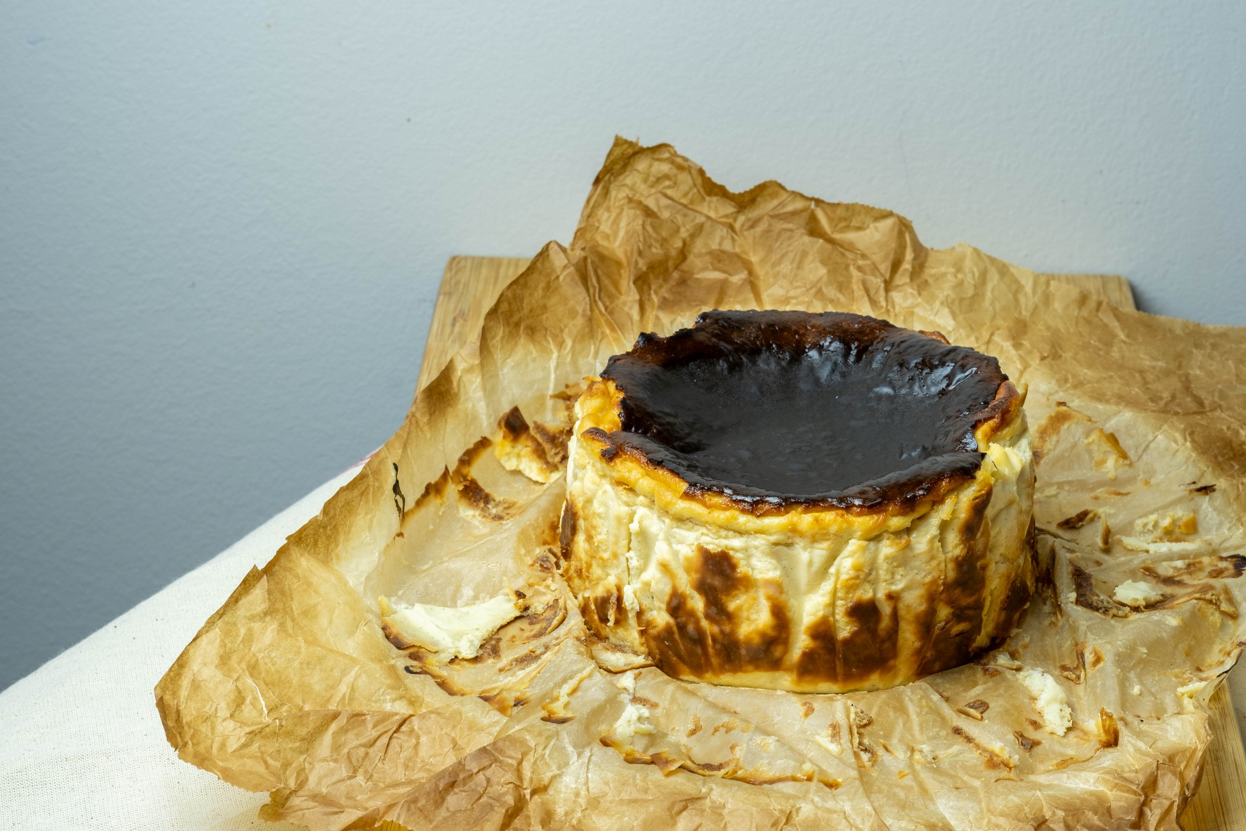 A piece of baked cheesecake with a dark caramelized top on crinkled parchment paper.