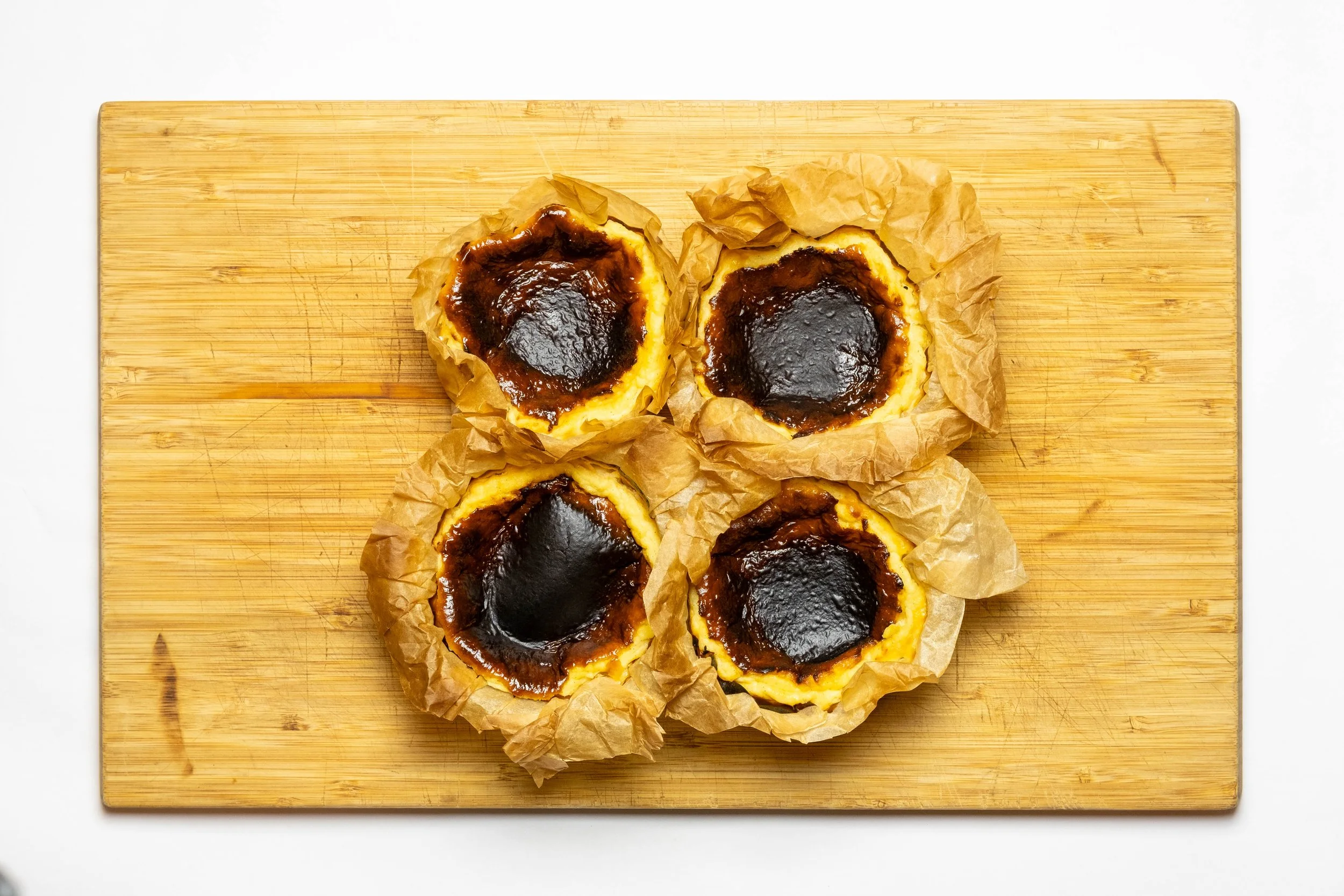 Four Bento Basque cheesecakes, wrapped in parchment paper, on a wooden cutting board.