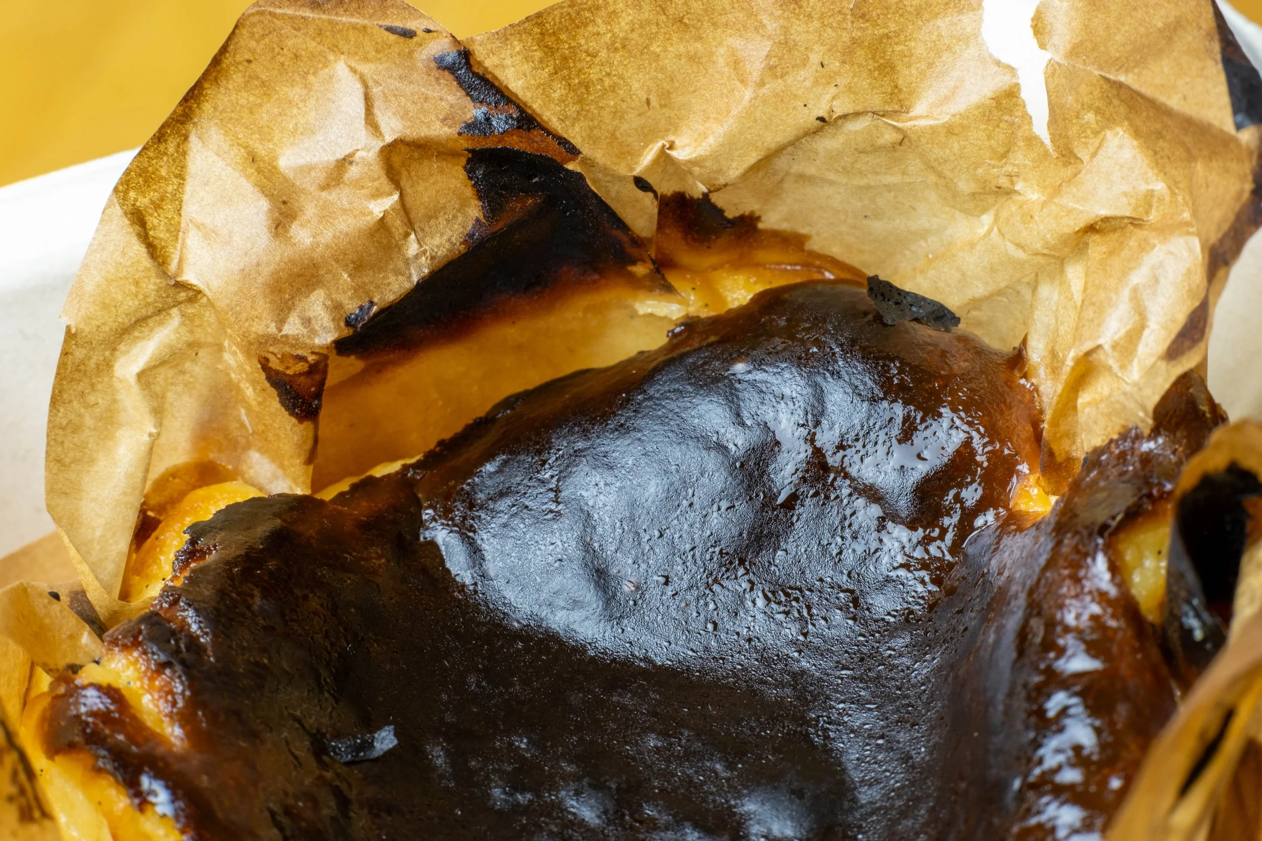 Close-up of a flame-broiled burger with melted cheese, topped with dark toasted bun, wrapped in crumpled brown paper.