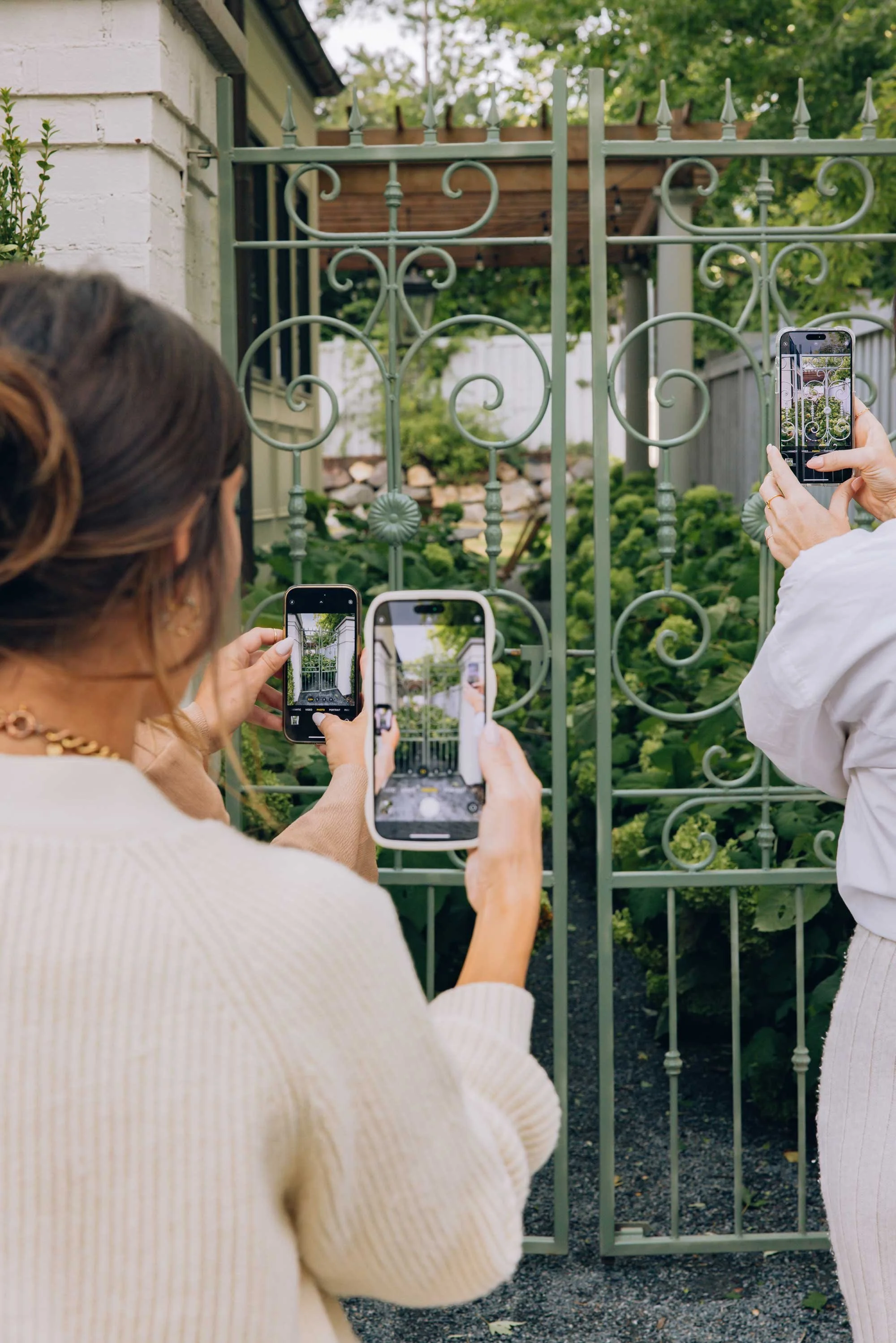 Avery Wagner social media agency strategist showing her phone and capturing content of a green gate and garden outside a home