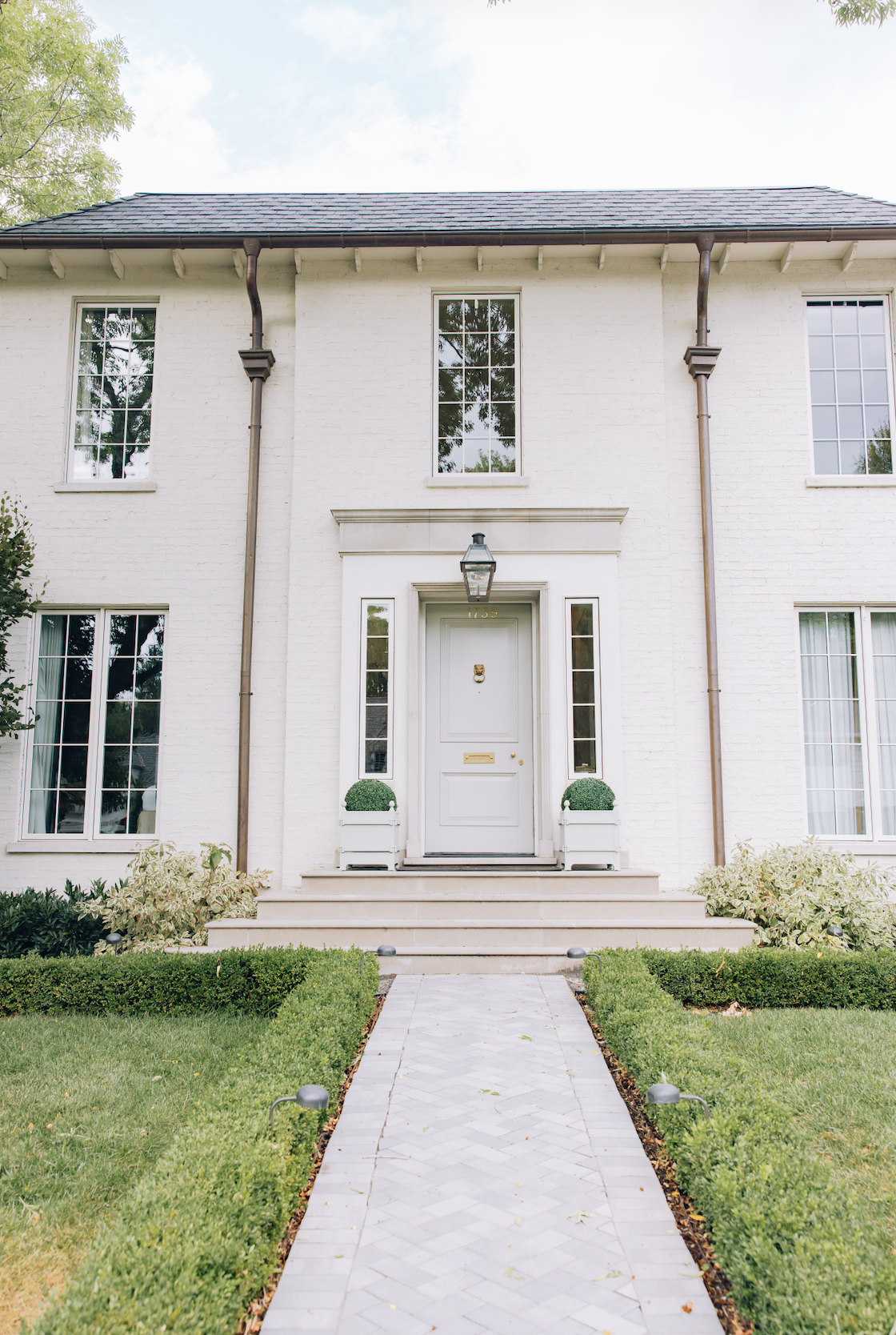White brick custom home with symmetrical windows, black roof, and landscaped front walkwa