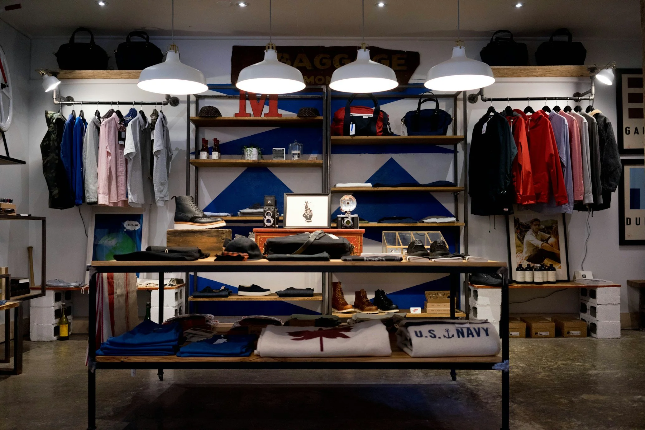Interior of a retail store displaying clothing, shoes, and accessories on shelves and hanging rods, with U.S. Navy items and military-themed decor.