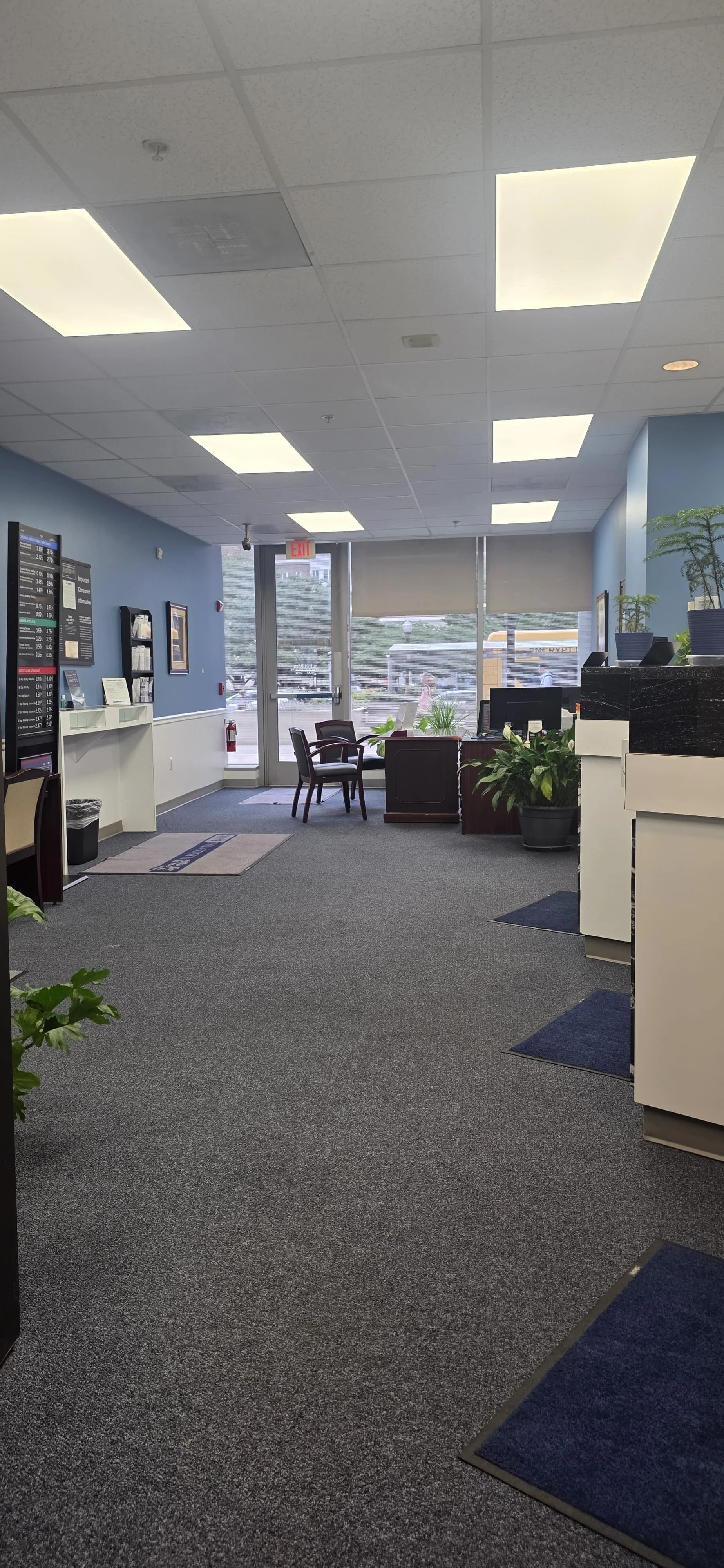 Empty office lobby with chairs, plants, a reception desk, and large windows.