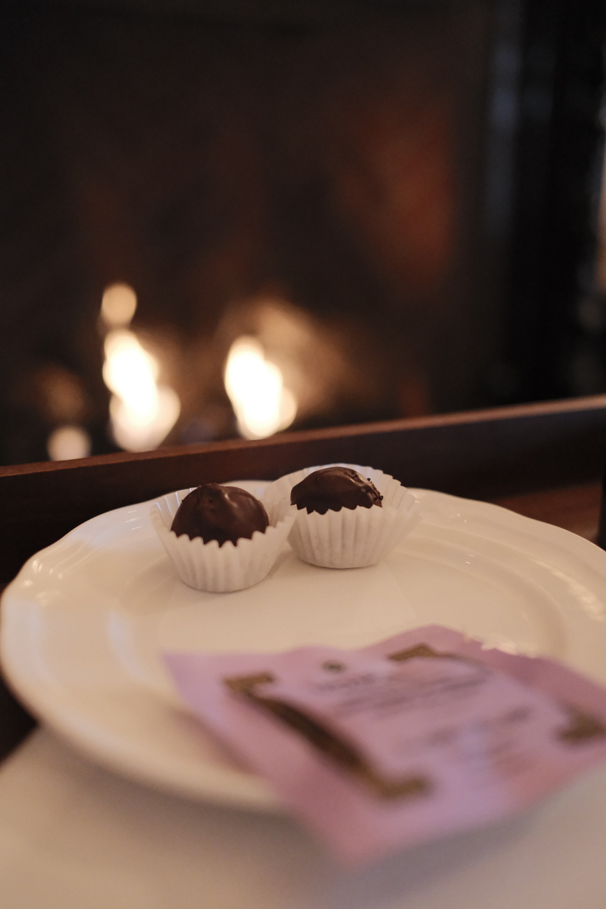 Two chocolate truffles on white plate in front of fireplace