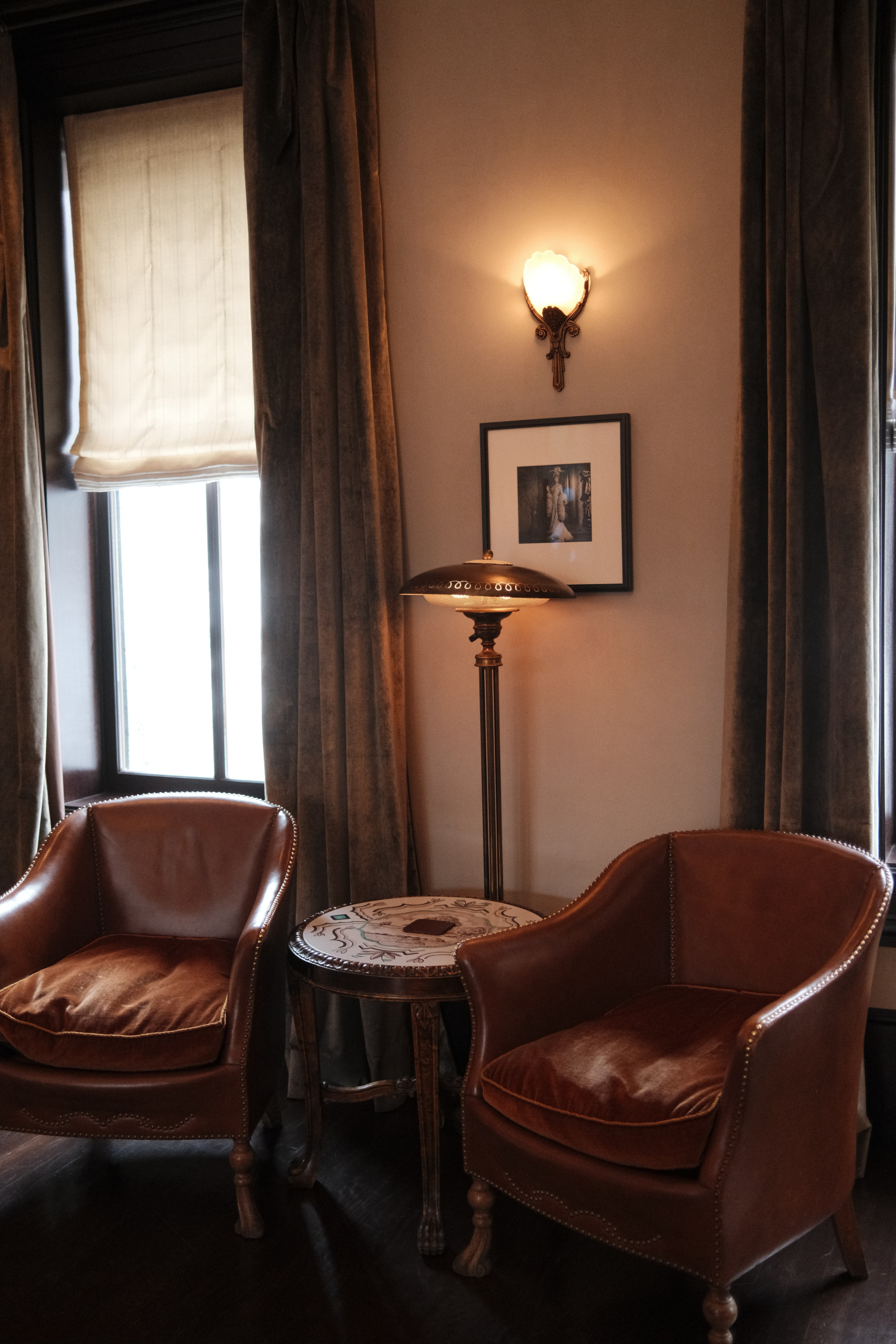 Two lounge chairs in the lobby with a drink table, floor lamp, art, and a window