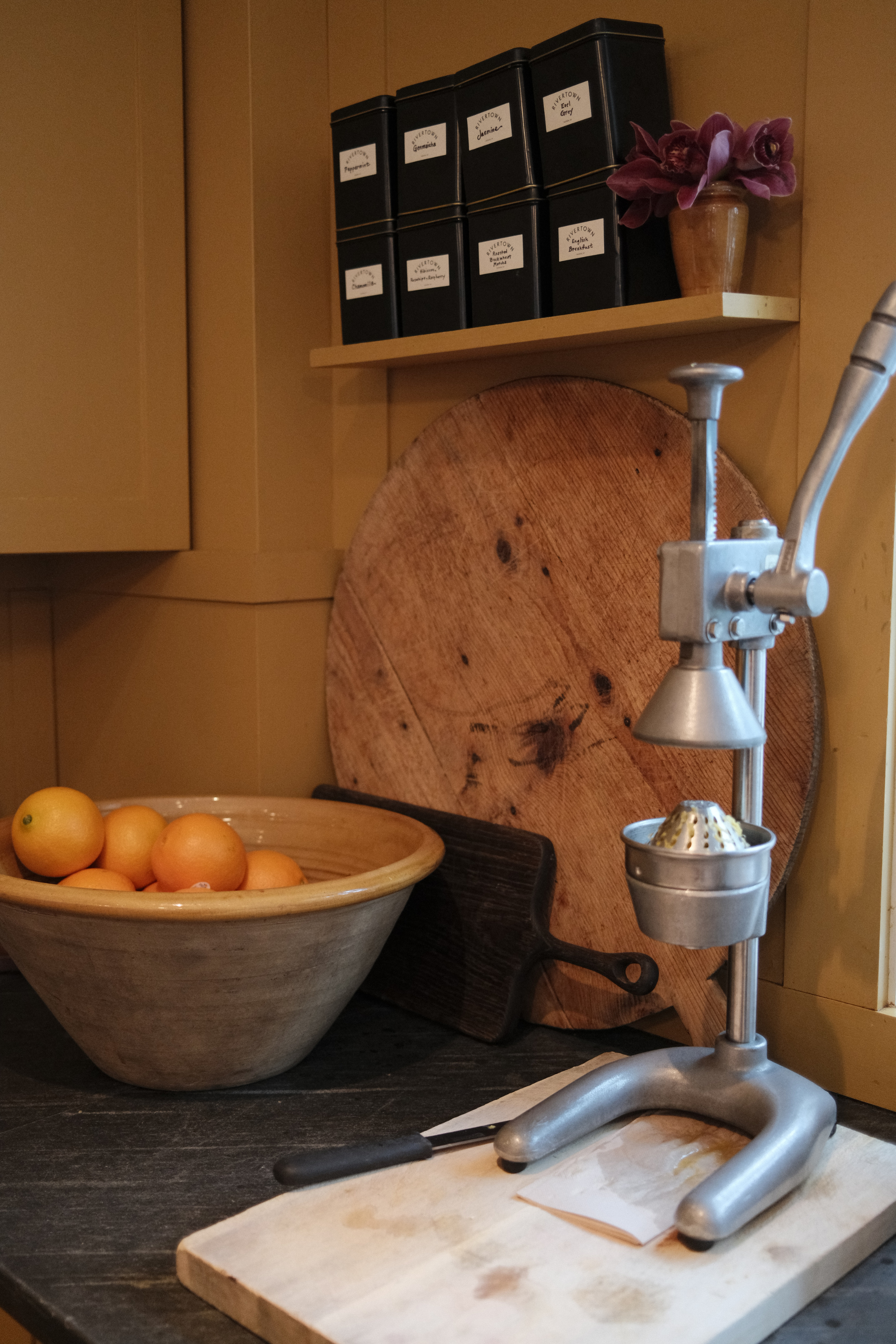 Lobby kitchen counter with a tea shelf and a bowl of oranges next to an orange press