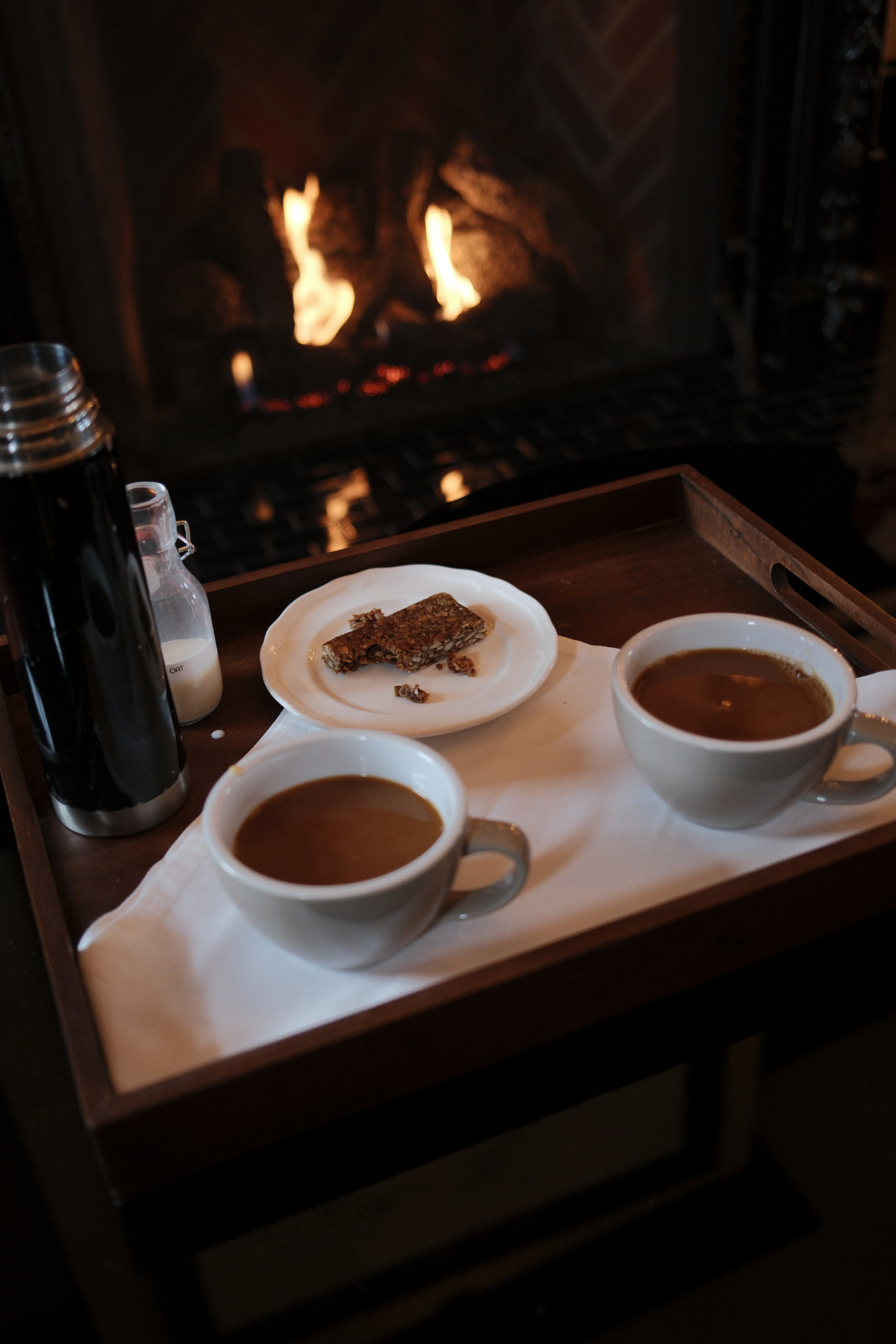 Two coffees and a granola bar in front of a fire