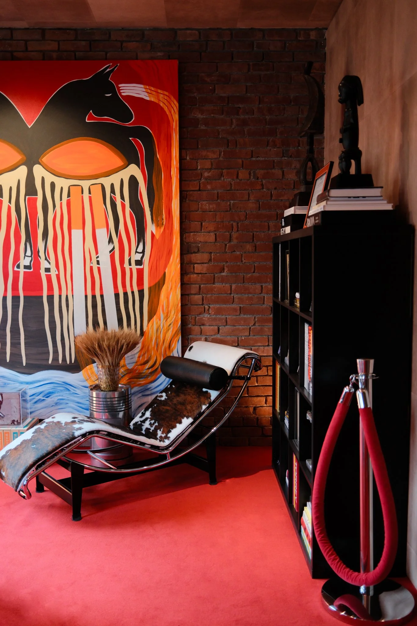 Room with red carpet, brick wall with large art, and cowhide chaise chair