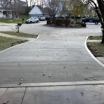 Concrete driveway leading to a residential street with parked cars and houses in the background.