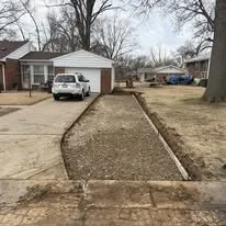 A driveway with a newly poured gravel sidewalk leading to a house with a white garage and a white pickup truck parked outside.
