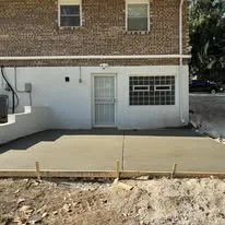 Front of a building with a door and a window, and a wooden frame on the sidewalk in front, possibly for a new concrete pour.
